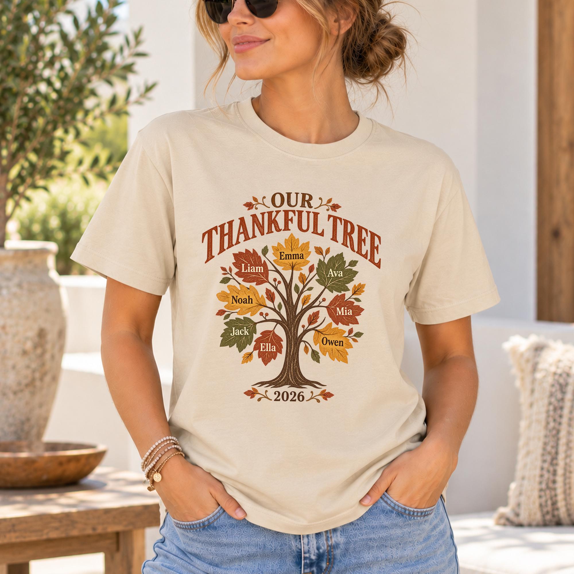 A woman wearing a white t-shirt with a graphic design of a tree with autumn leaves and the text "Our Thankful Tree" printed on it.