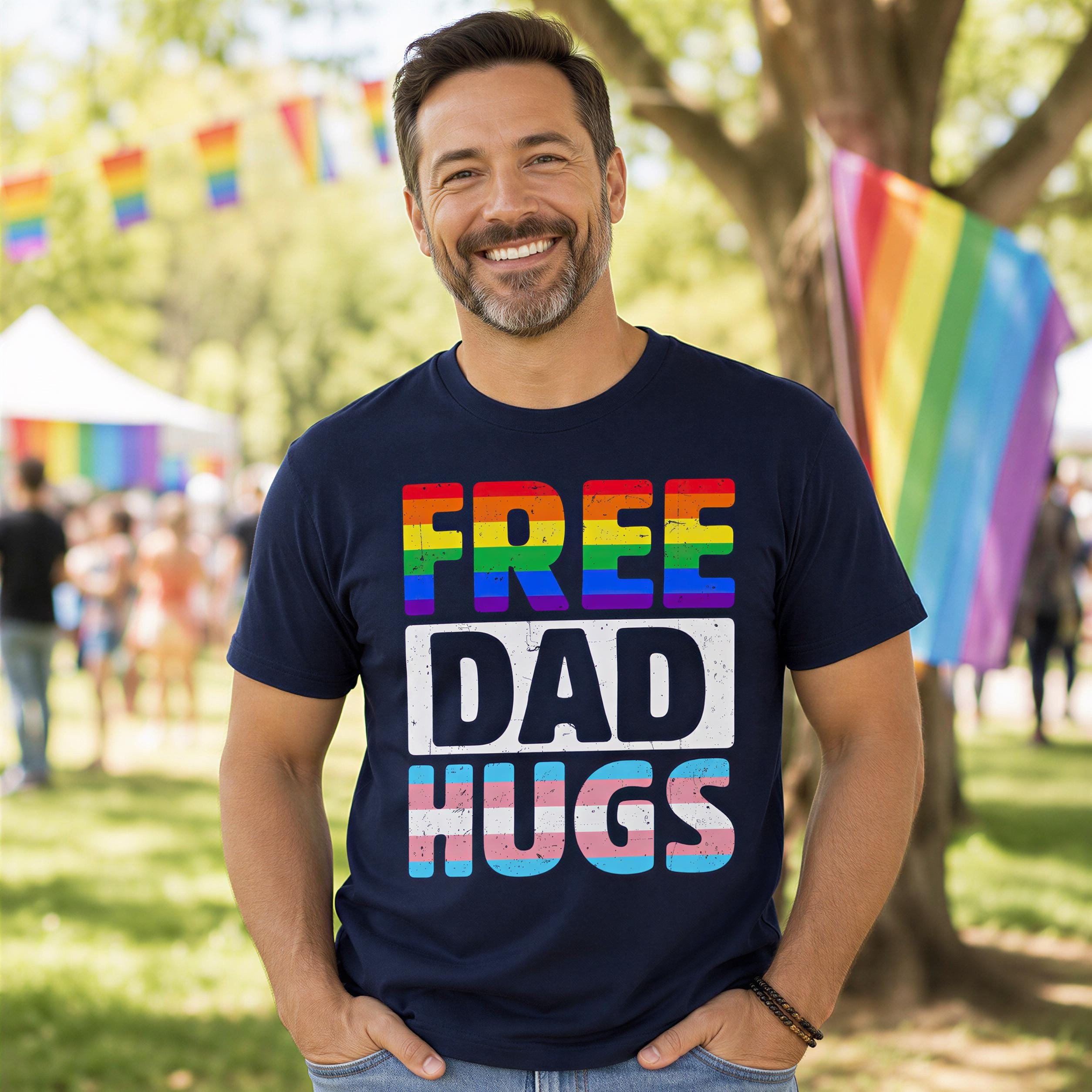 A man wearing a black t-shirt with rainbow text and graphics stands in a park, smiling at the camera.