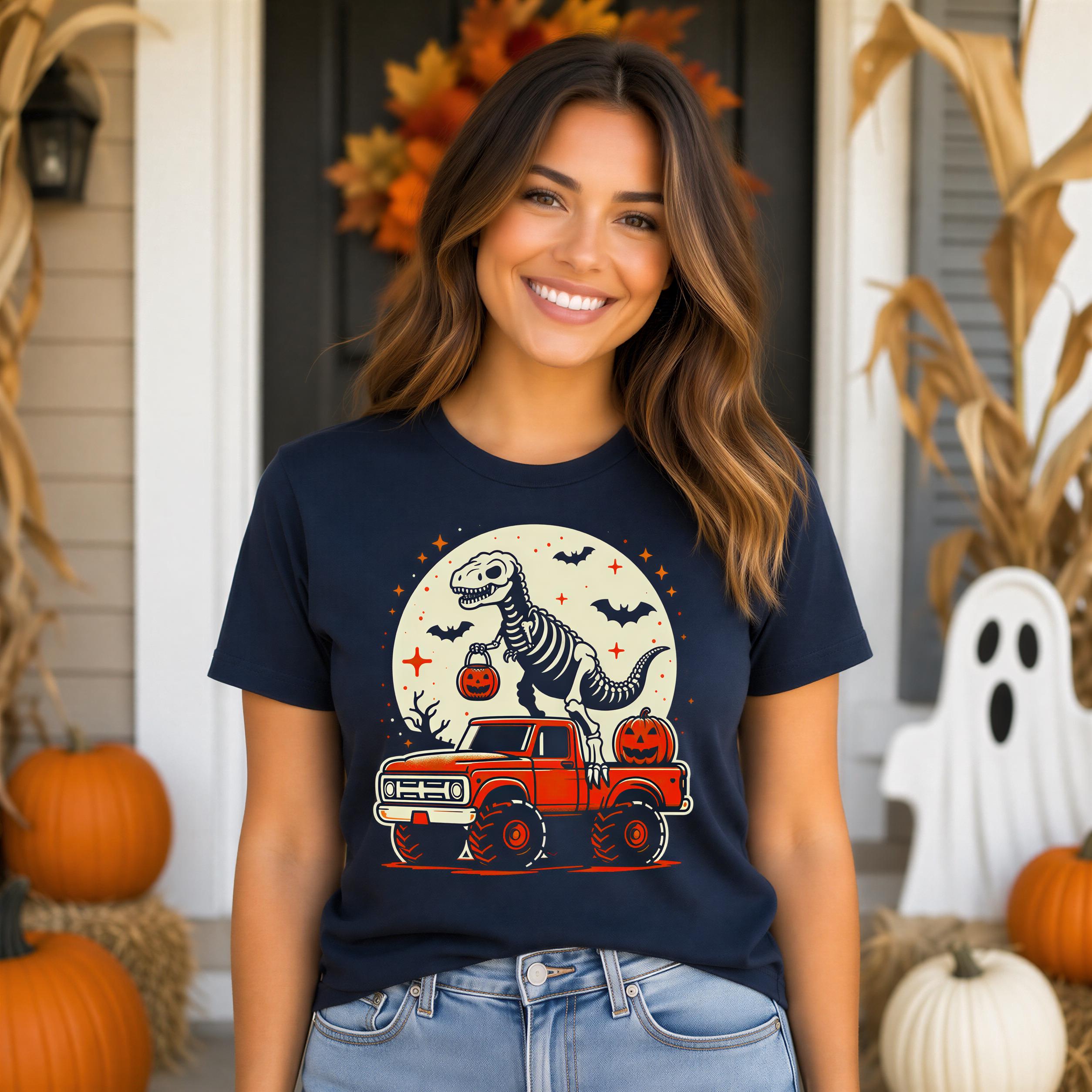 A woman wearing a navy blue t-shirt with a graphic of a skeleton dinosaur riding a red truck, holding a jack-o-lantern, and a full moon with bats, standing in front of a house decorated for Halloween.