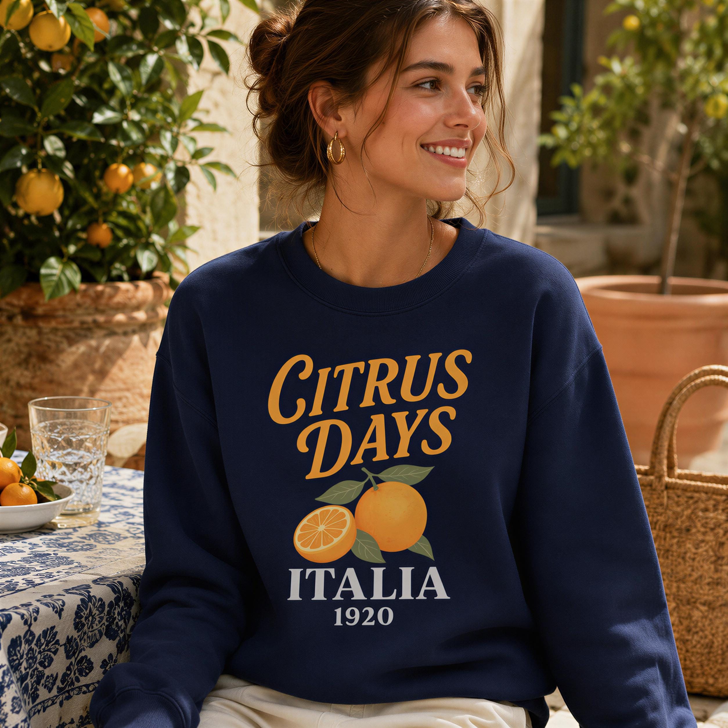 A woman wearing a navy blue sweatshirt with the text "CITRUS DAYS ITALIA 1920" printed on it, smiling and looking to the side.