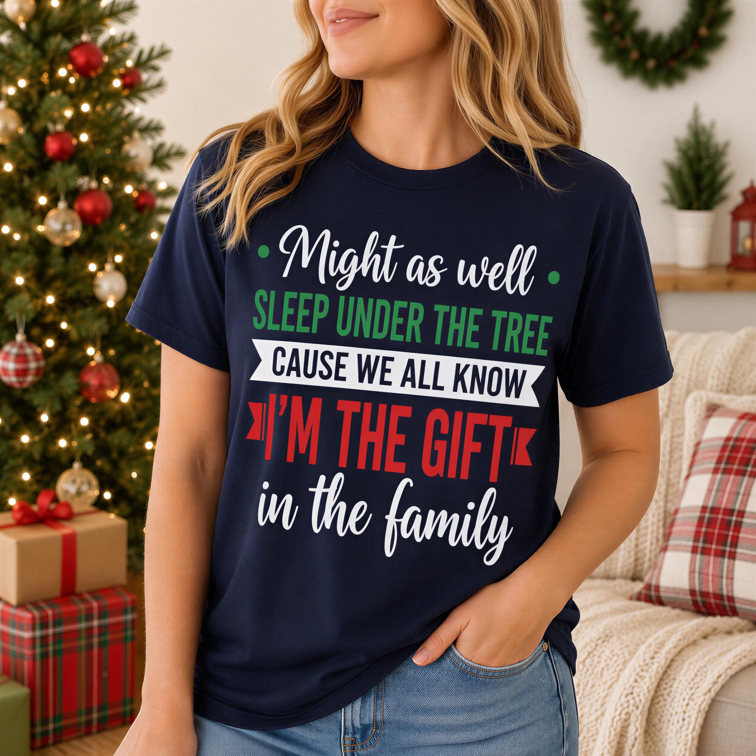 A woman wearing a navy blue t-shirt with a humorous Christmas-themed text printed on it, standing in front of a Christmas tree.
