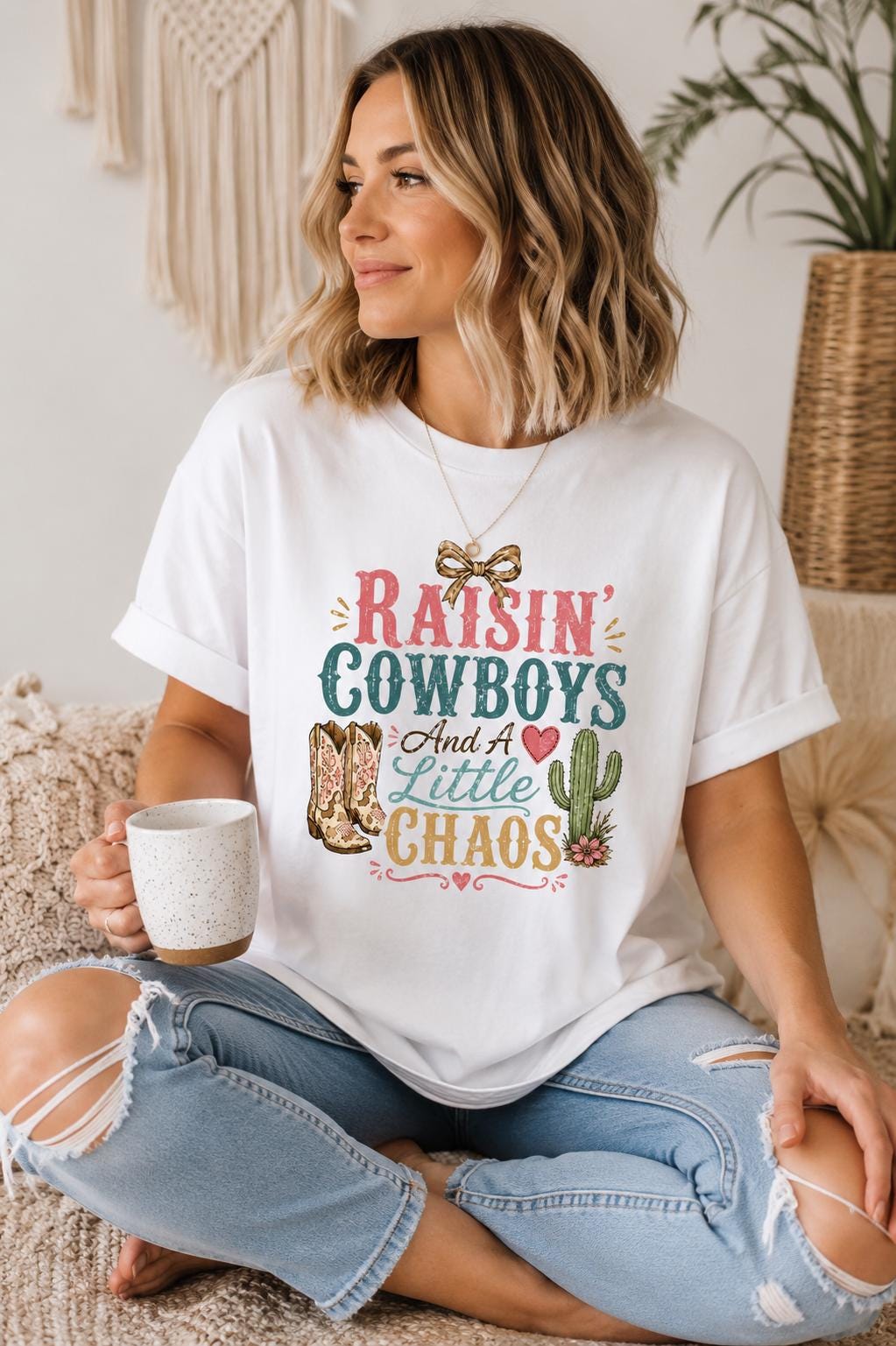A woman sitting on a couch, wearing a white t-shirt with a colorful graphic design and holding a coffee mug.