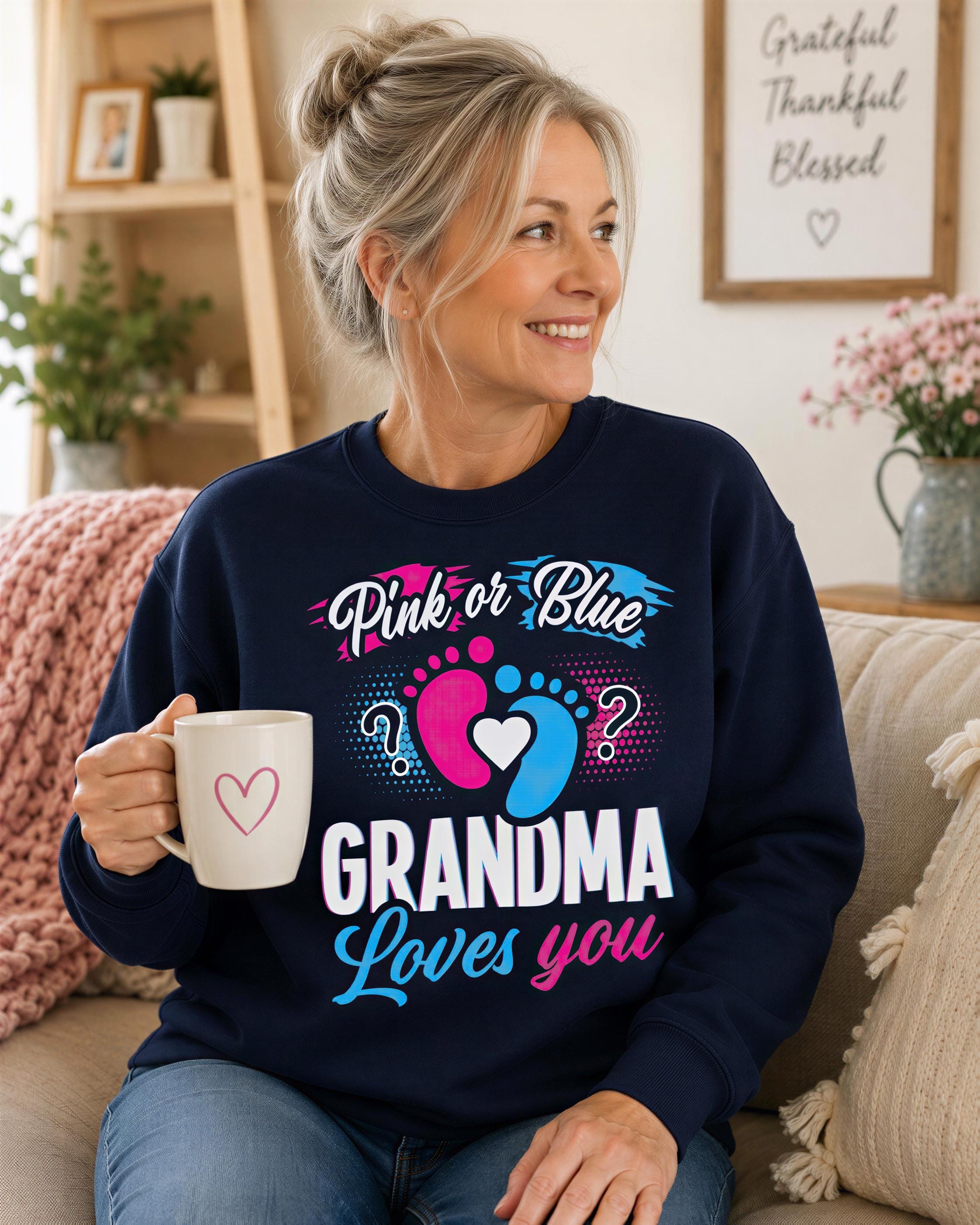A woman sitting on a couch, holding a coffee mug, and wearing a sweater with a pink or blue design that says "Grandma loves you".