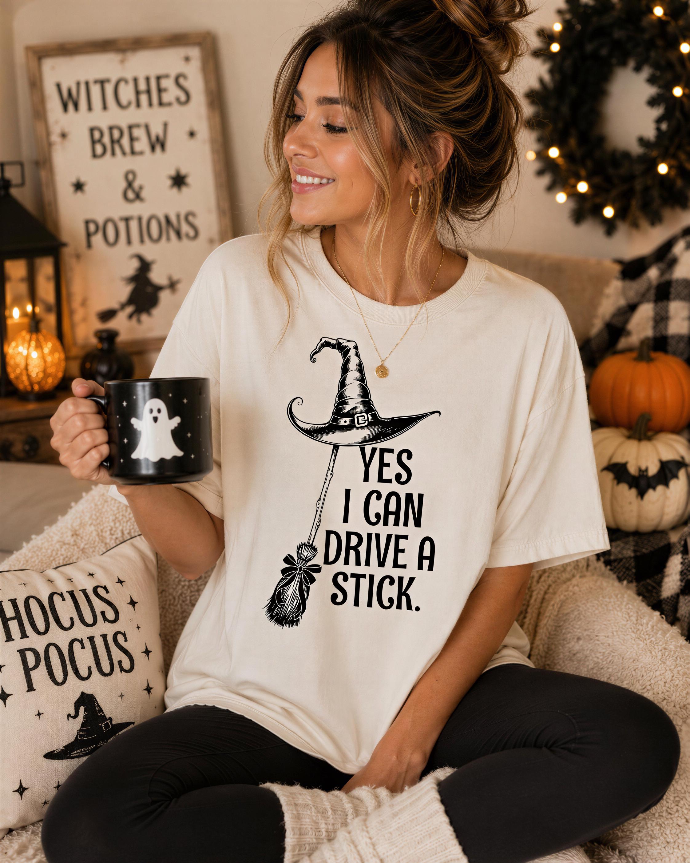 A woman wearing a white t-shirt with a graphic of a witch's broom and a mug with a ghost design, sitting on a couch and smiling.