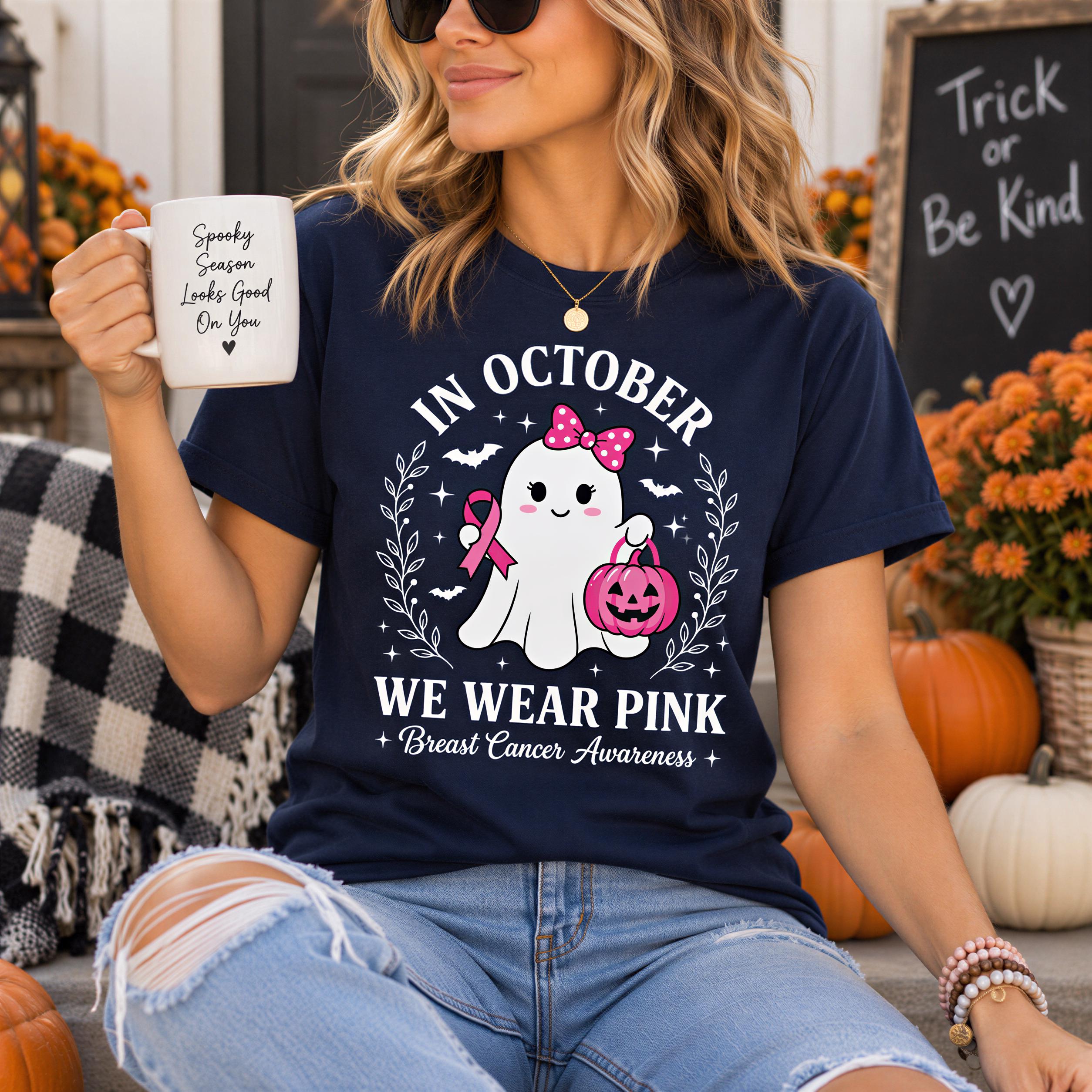 A woman wearing a navy blue t-shirt with a graphic design and text, holding a white mug with a message, and surrounded by pumpkins and flowers.