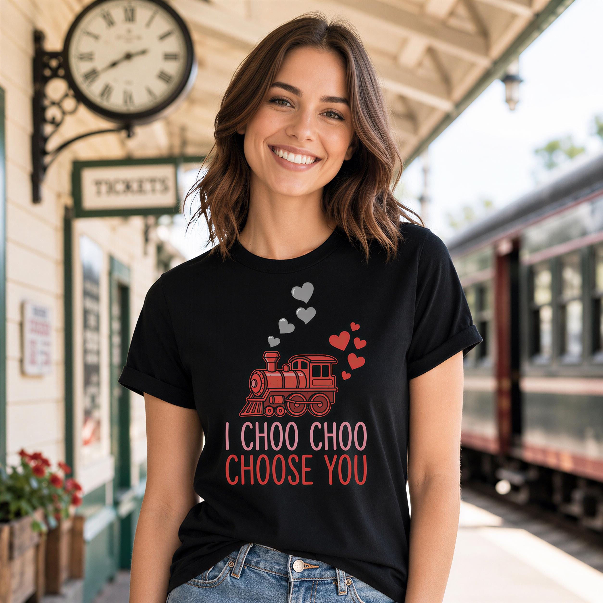 A woman wearing a black t-shirt with a graphic of a train and the text "I choo choo choose you" is standing in front of a train station.