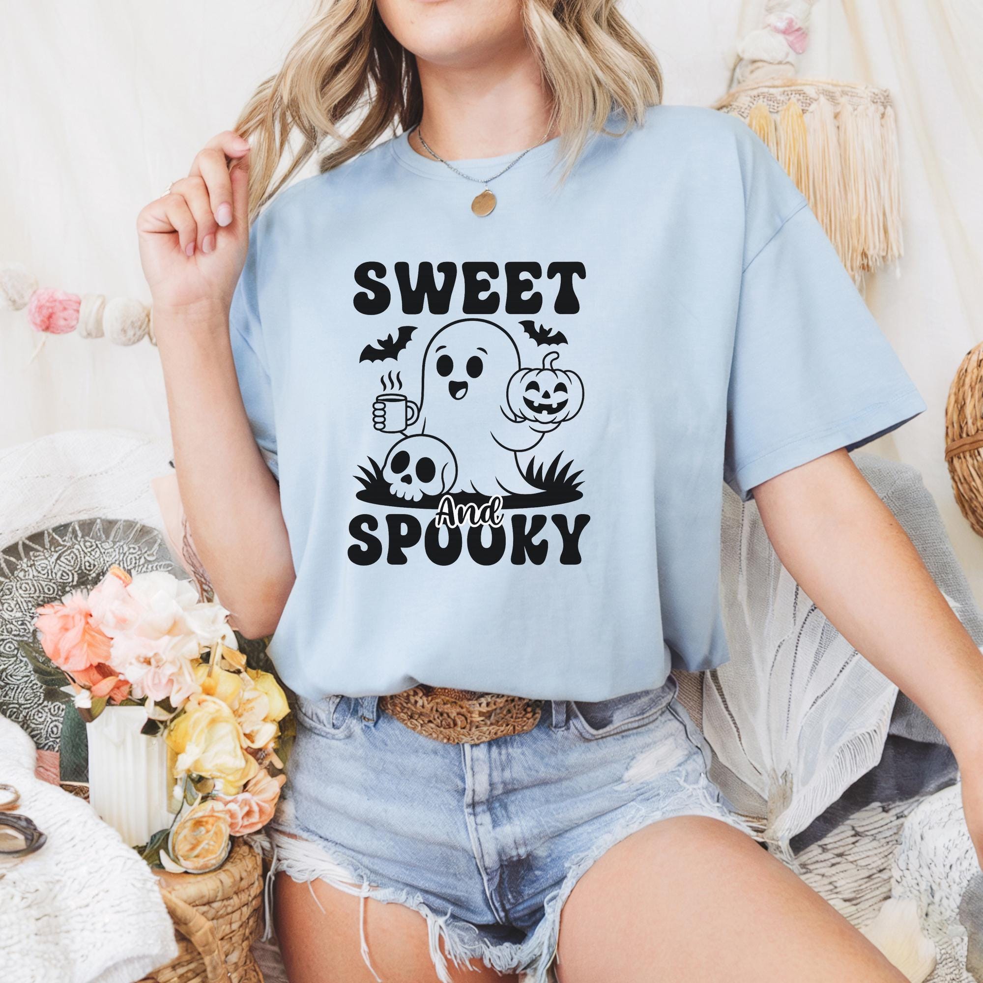 A woman wearing a light blue t-shirt with a graphic design featuring a ghost, pumpkin, and the text "Sweet and Spooky".