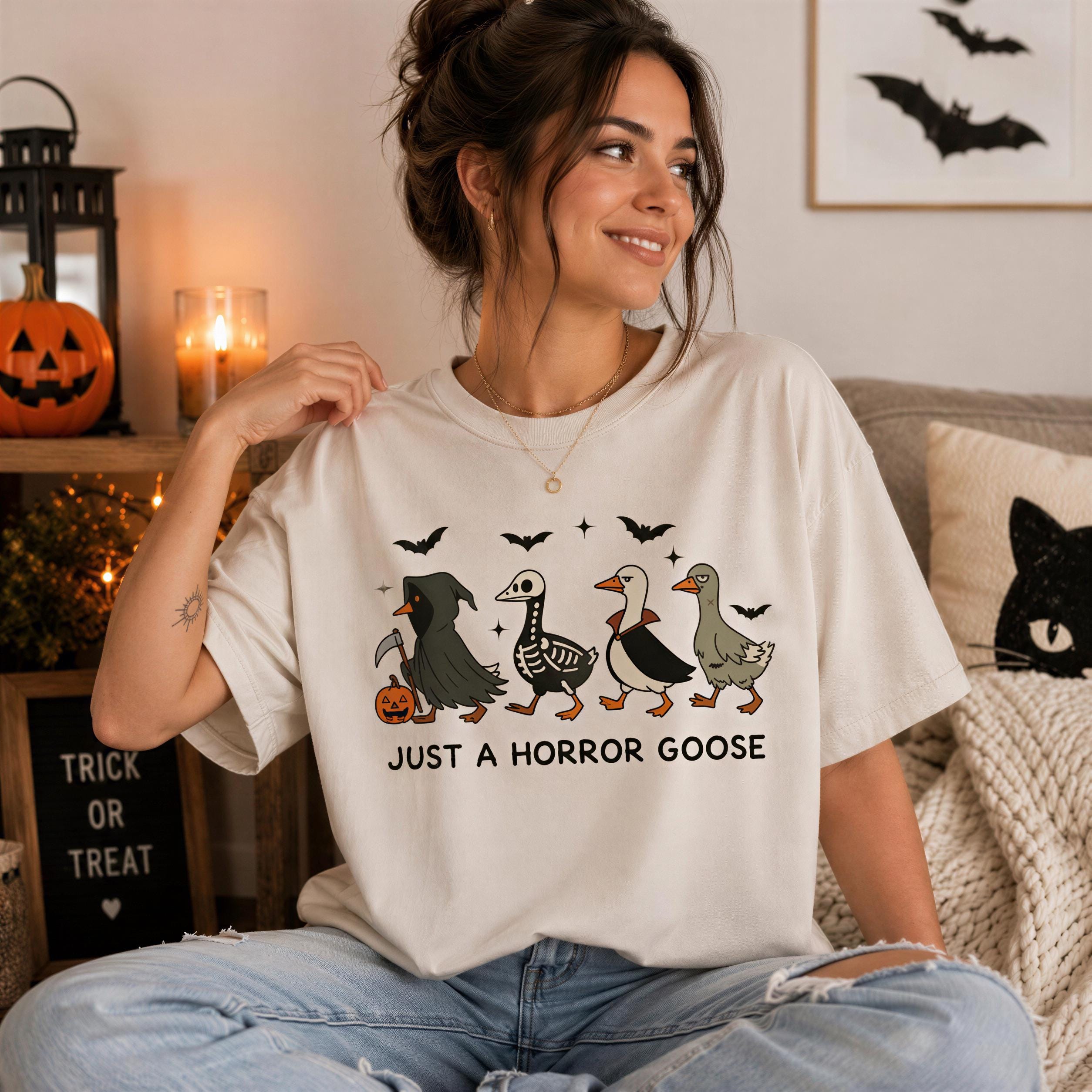 A woman wearing a white t-shirt with a graphic of a group of birds, including a goose, and the text "Just a Horror Goose" is sitting on a couch.