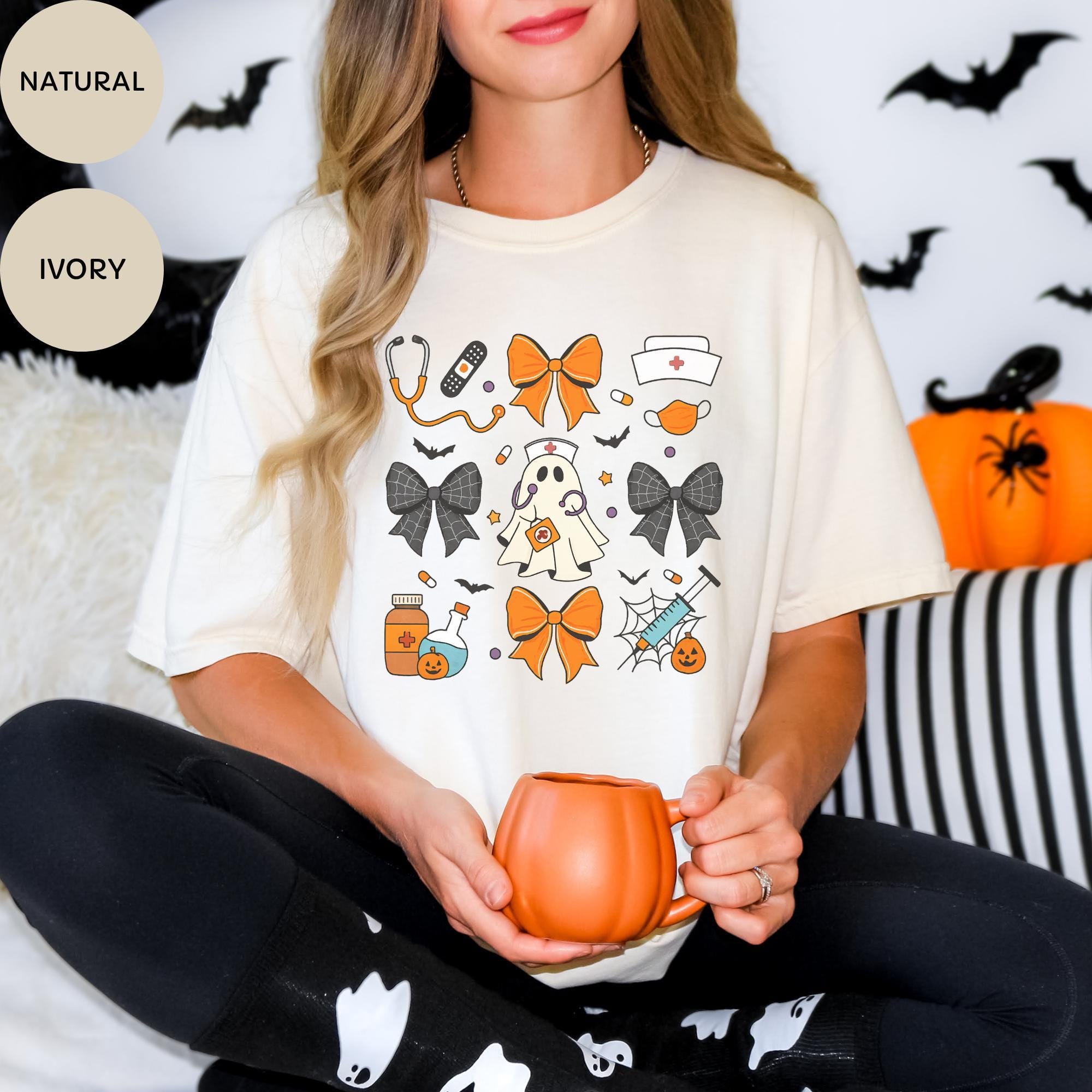 A woman wearing a white t-shirt with a Halloween-themed graphic design, holding a pumpkin-shaped mug, and sitting on a bed with Halloween decorations in the background.