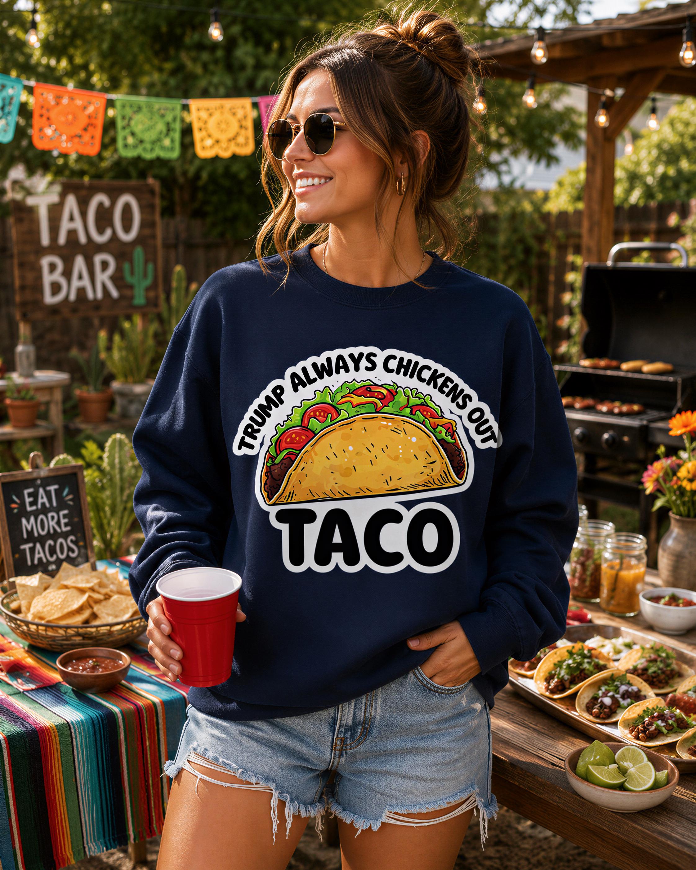 A woman wearing a blue sweatshirt with a graphic of a taco and the text "Trump always chickens out taco" is standing in front of a table with various food items, including a large bowl of tortilla chips and a plate of tacos.