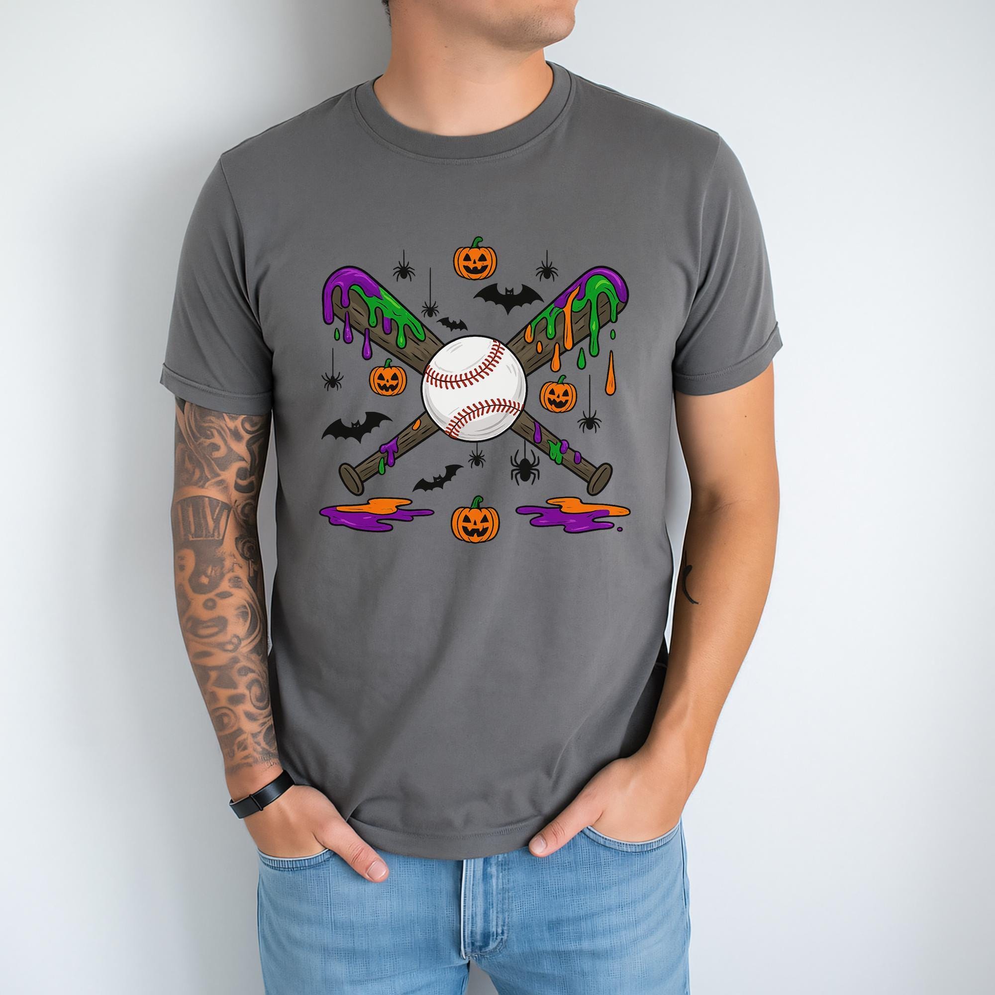 A man wearing a gray t-shirt with a graphic design featuring a baseball bat, pumpkins, bats, and a baseball.
