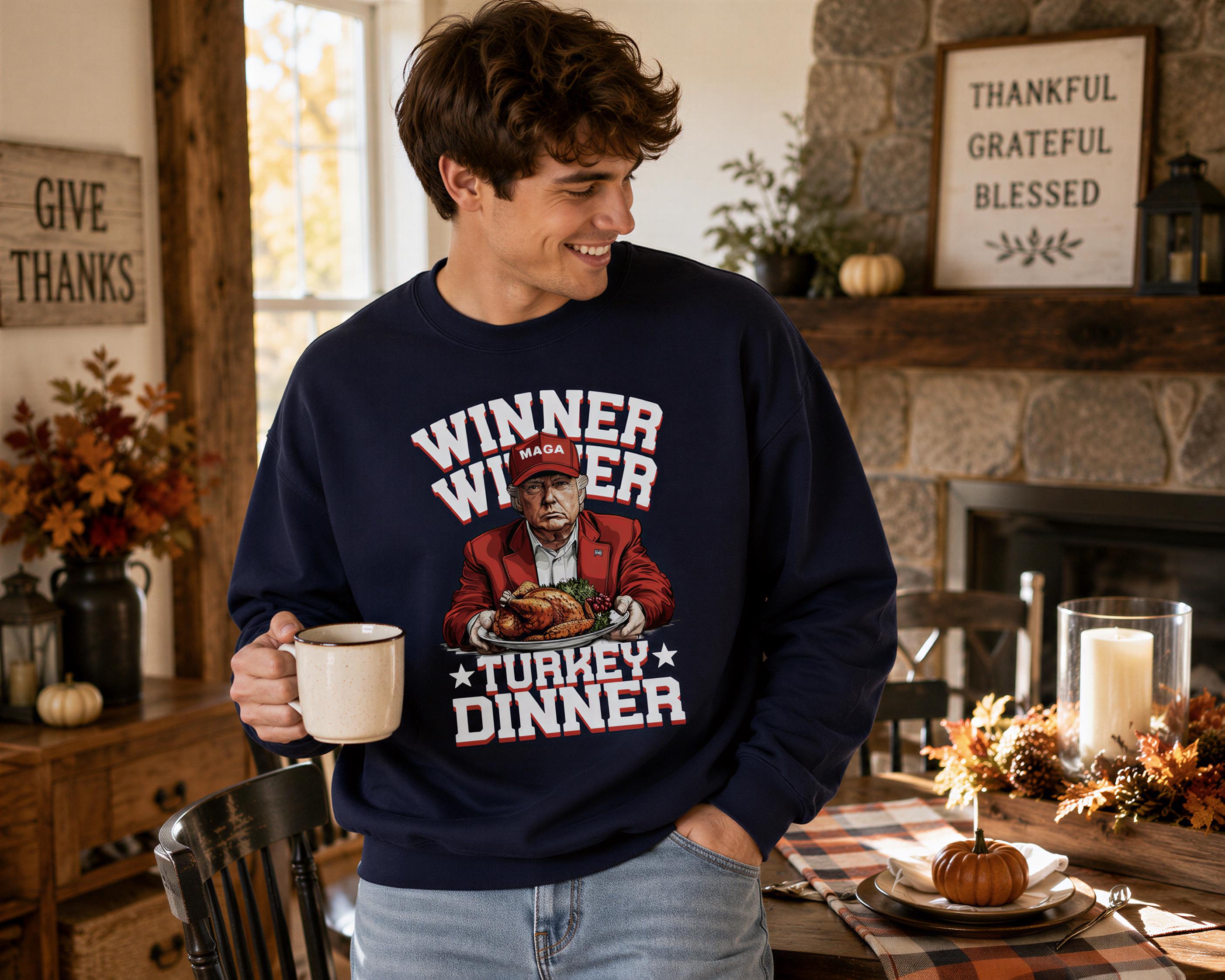 A man wearing a navy blue sweatshirt with a graphic of a man holding a turkey and the text "WINNER WINNER TURKEY DINNER" is smiling and holding a coffee mug in a cozy, autumn-themed room.