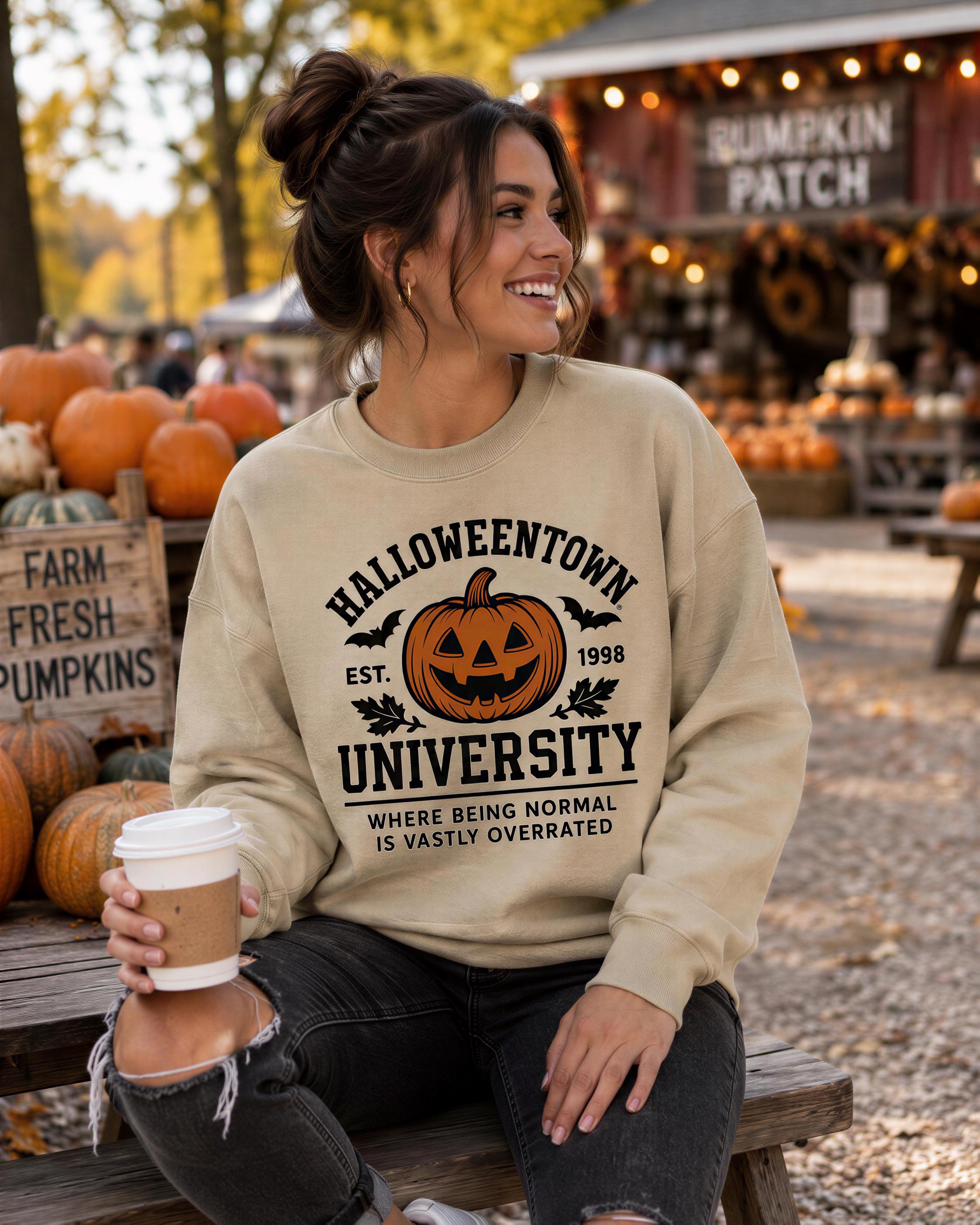 A woman wearing a Halloween-themed sweatshirt is sitting on a wooden bench, holding a coffee cup, with a pumpkin patch and fall decorations visible in the background.