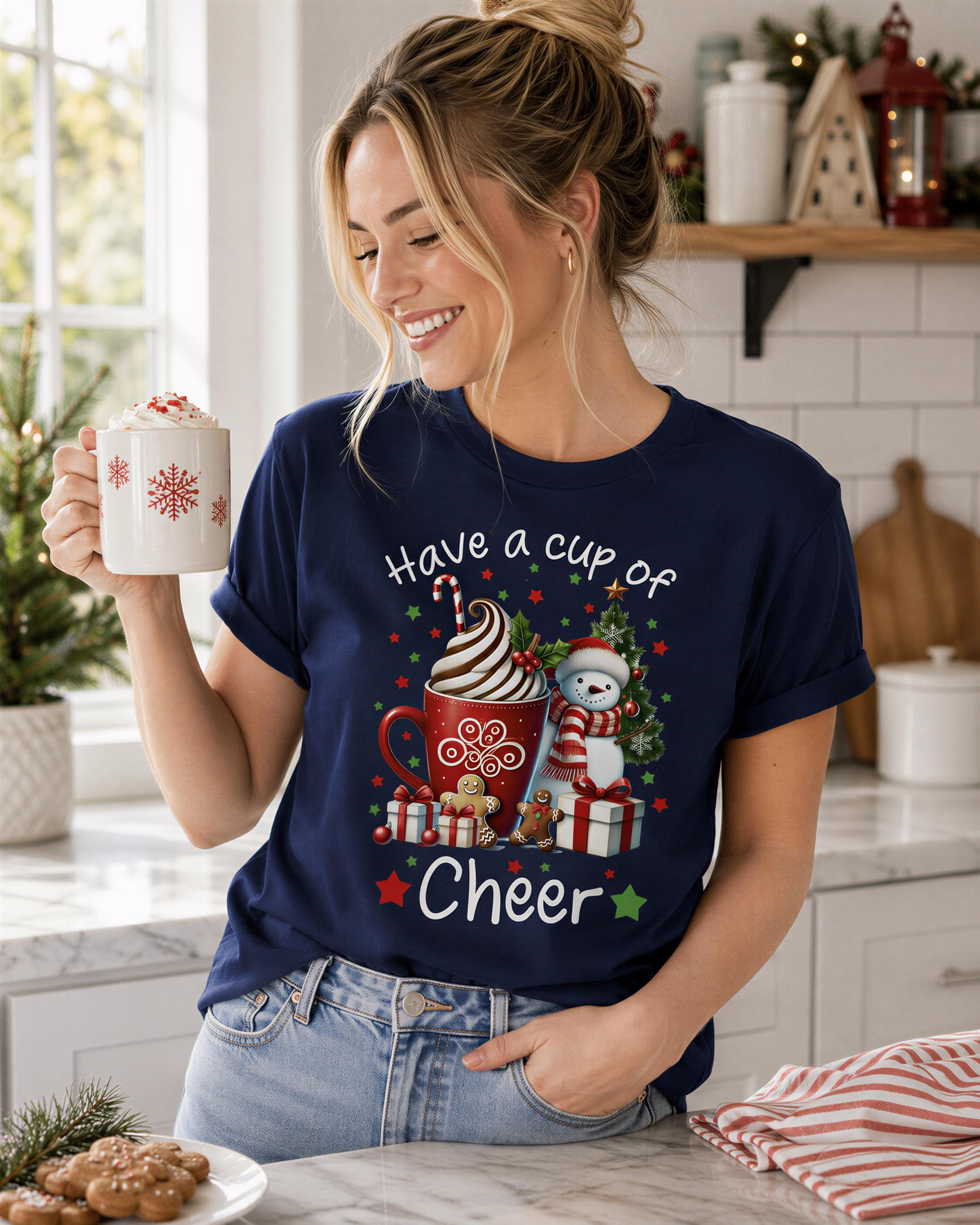 A woman is holding a mug with a festive design, including a cup of coffee, a snowman, and Christmas presents, while smiling and posing in a kitchen setting.