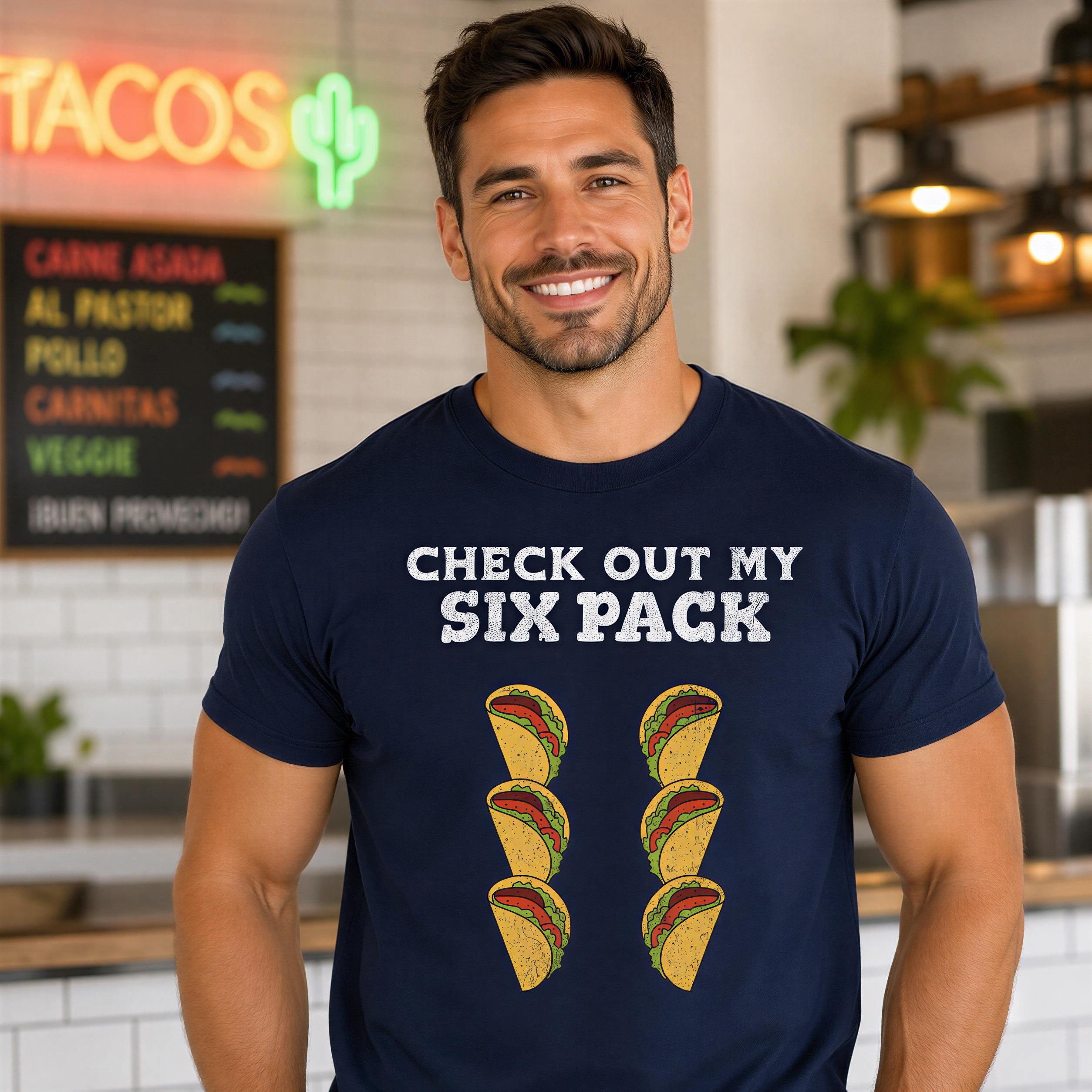 A man wearing a navy blue t-shirt with the text "CHECK OUT MY SIX PACK" and images of six tacos smiling at the camera.