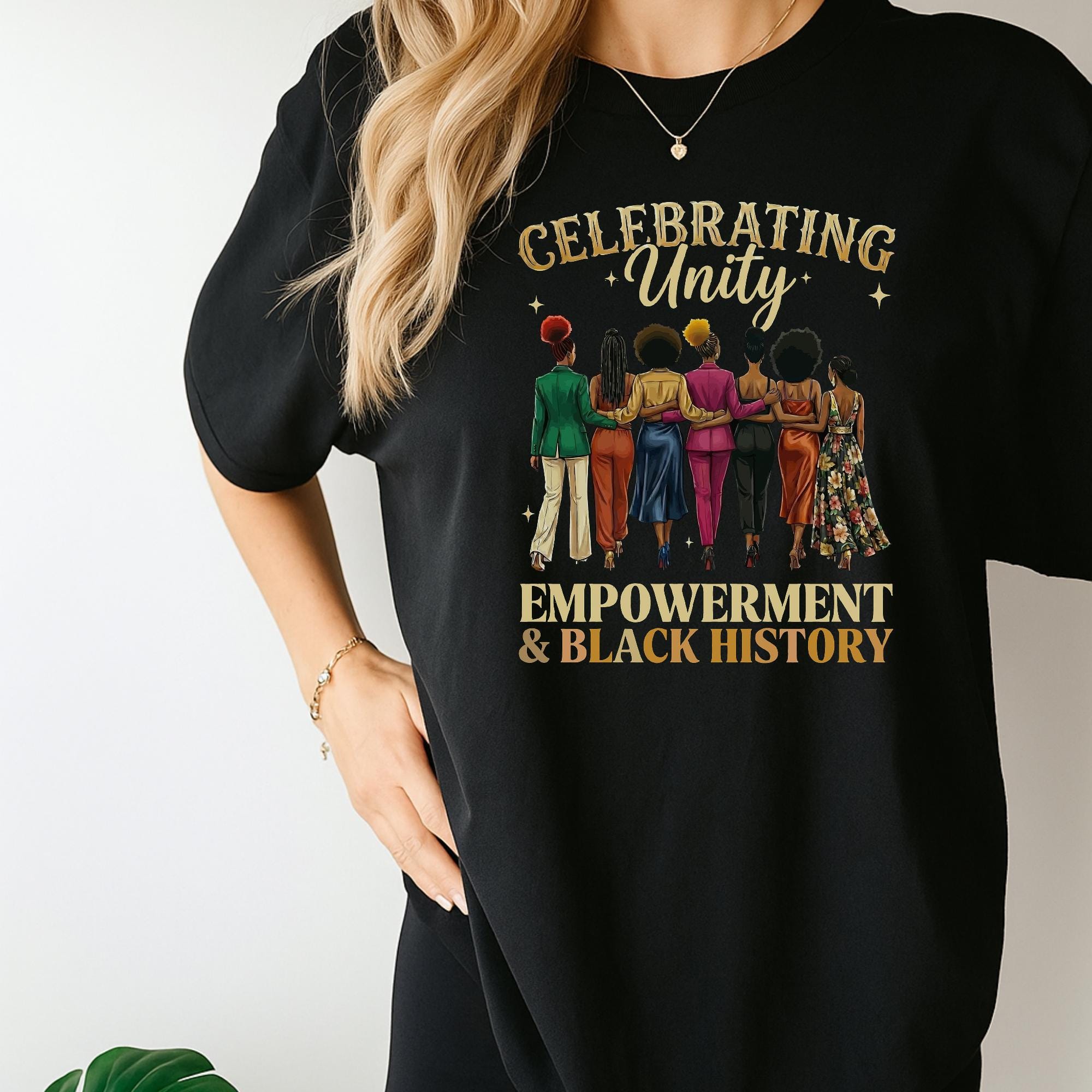A person wearing a black t-shirt with a graphic design featuring a group of diverse women and the text "Celebrating Unity Empowerment & Black History".