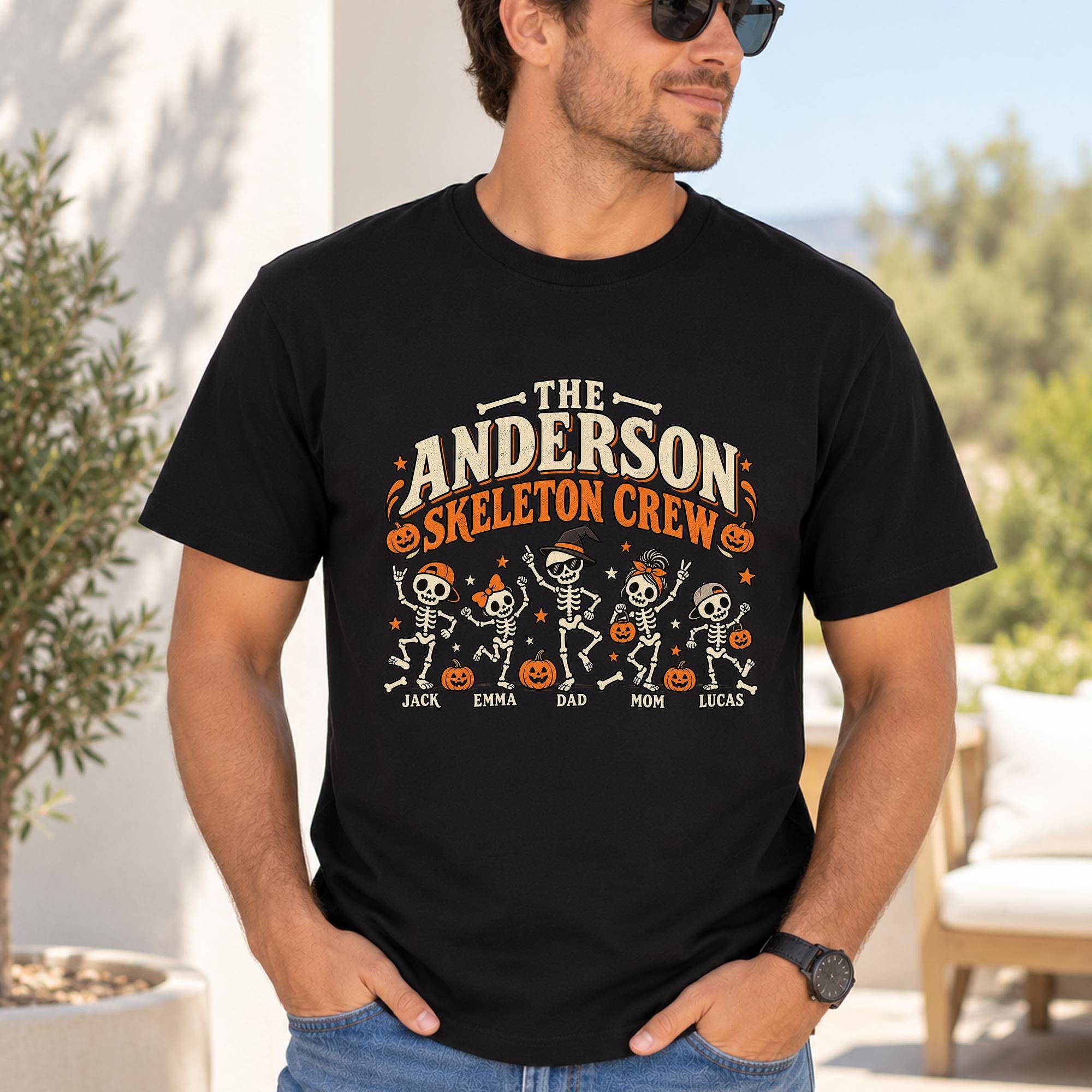 A man wearing a black t-shirt with a Halloween-themed graphic design featuring a skeleton crew and their names.