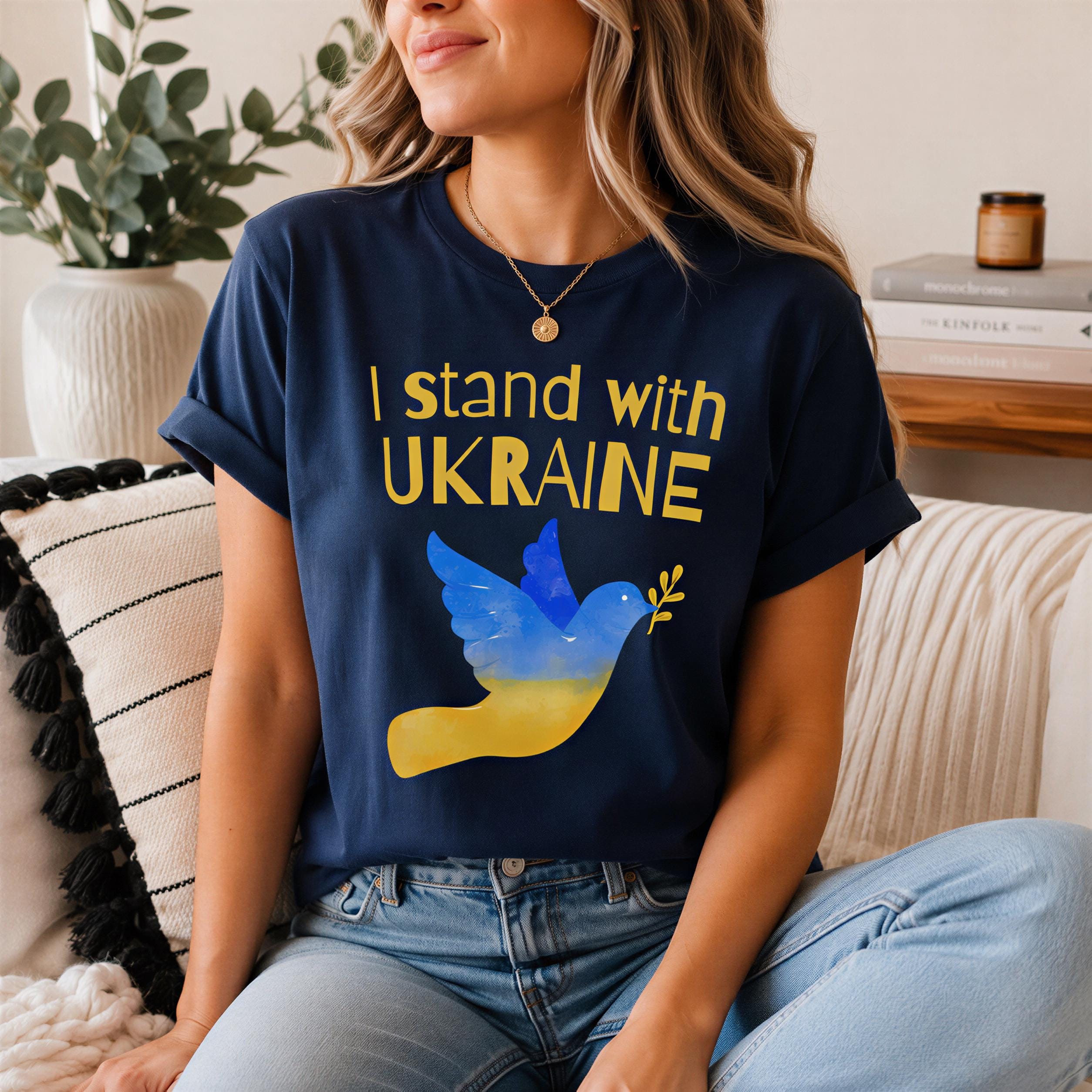 A woman wearing a blue t-shirt with a graphic of a bird and the text "I stand with Ukraine" is sitting on a couch.