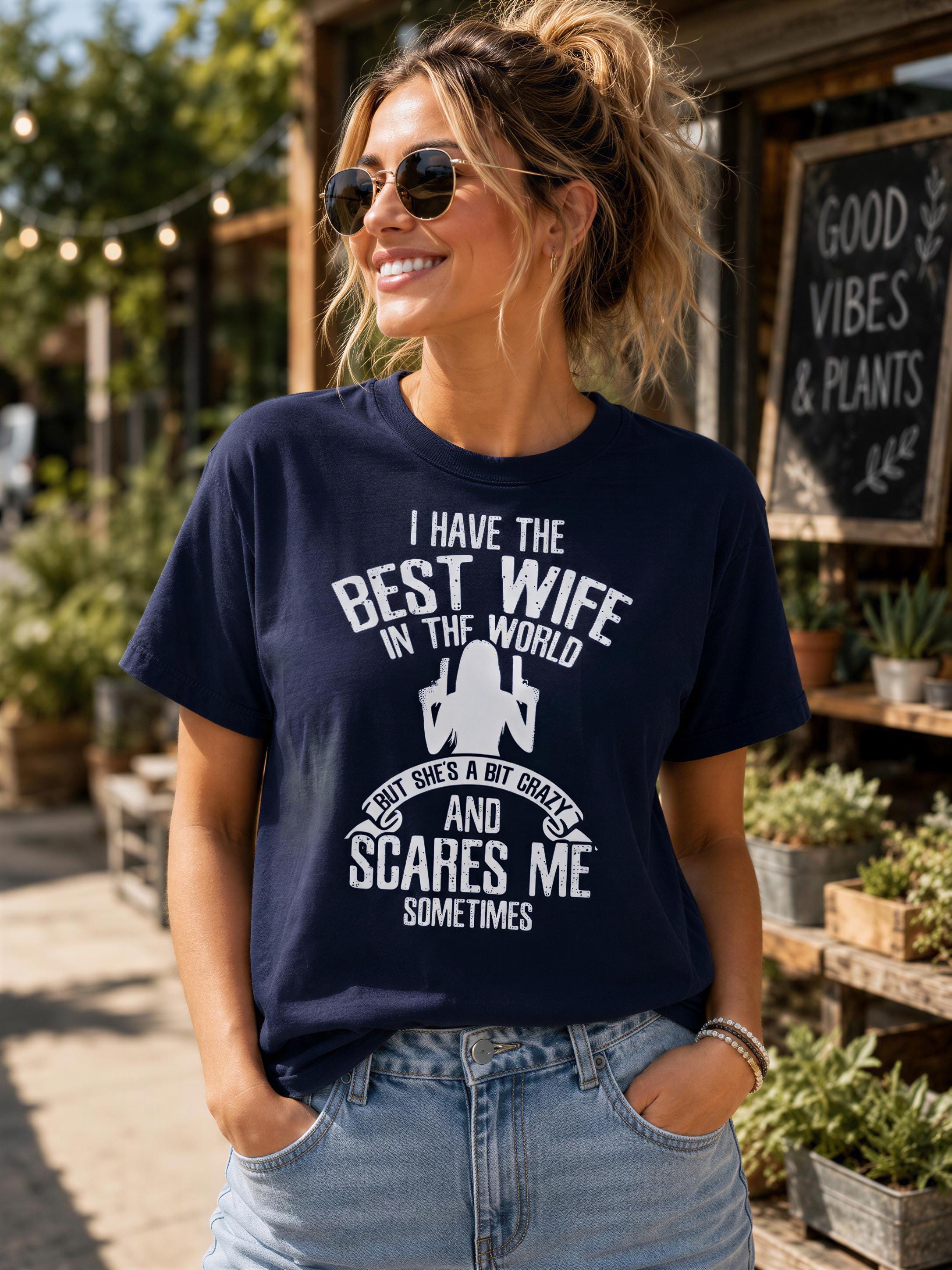 A woman wearing a navy blue t-shirt with a humorous text printed on it, smiling and posing in front of a storefront.