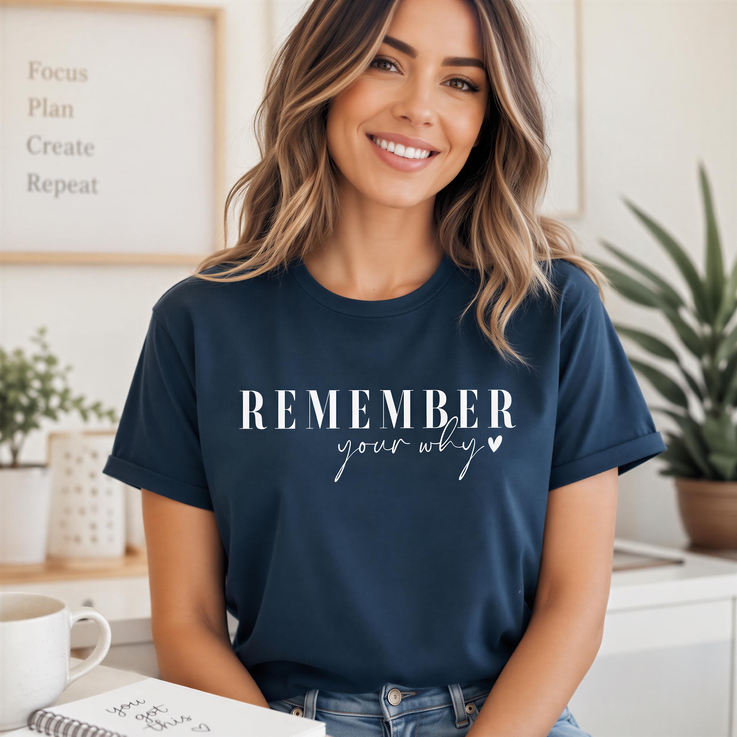 A woman wearing a navy blue t-shirt with the text "Remember your why" is smiling and posing for the camera.