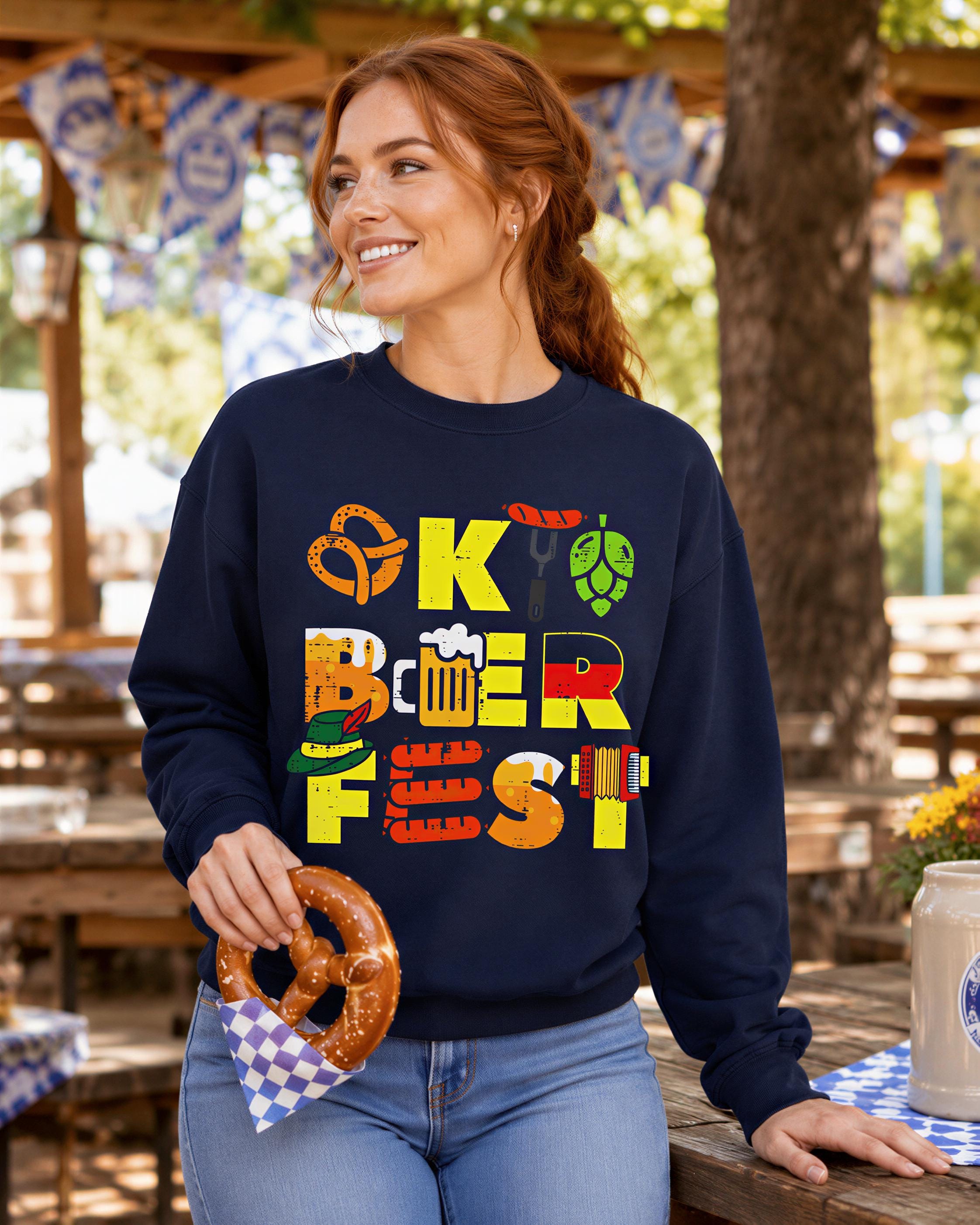 A woman wearing a navy blue sweatshirt with a graphic design of various beer-related icons and text, smiling and holding a pretzel.