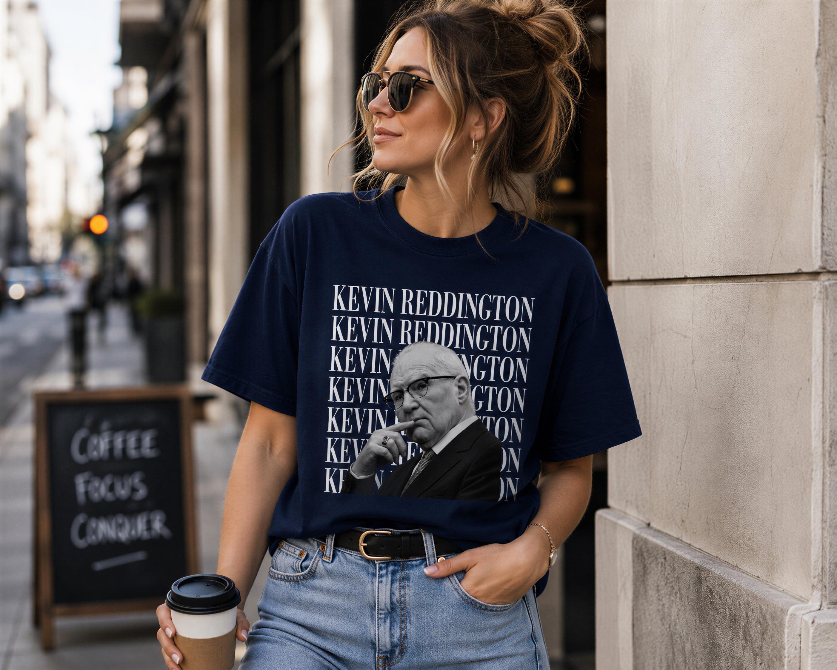 A woman wearing a navy blue t-shirt with a graphic of a man and holding a coffee cup, standing on a city street.