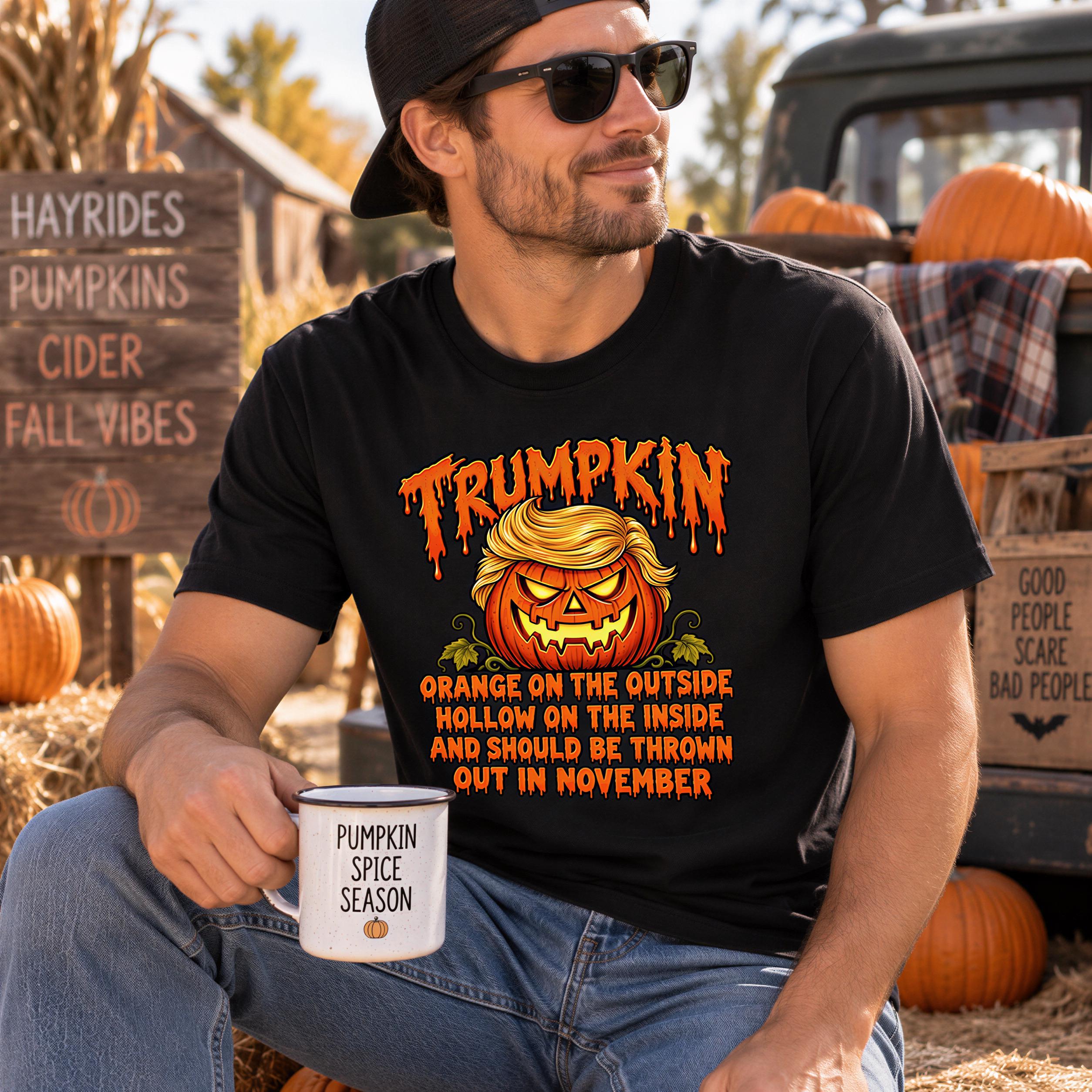 A man wearing a black t-shirt with a pumpkin graphic and text, sitting in front of a truck with a sign that says "HAYRIDES PUMPKINS CIDER FALL VIBES" and multiple pumpkins.