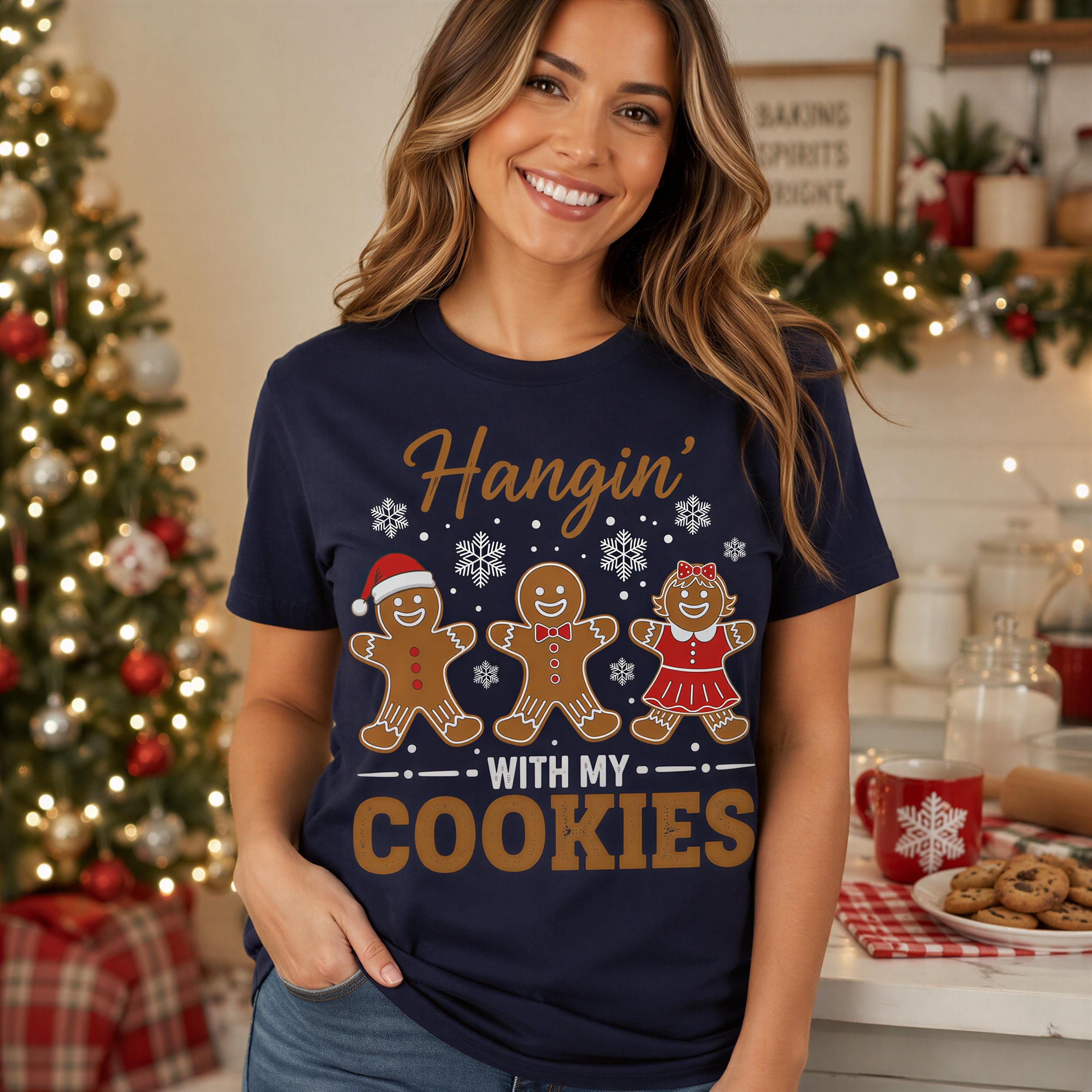 A smiling woman wearing a navy blue t-shirt with a graphic design of gingerbread men and the text "Hanging in with my cookies".