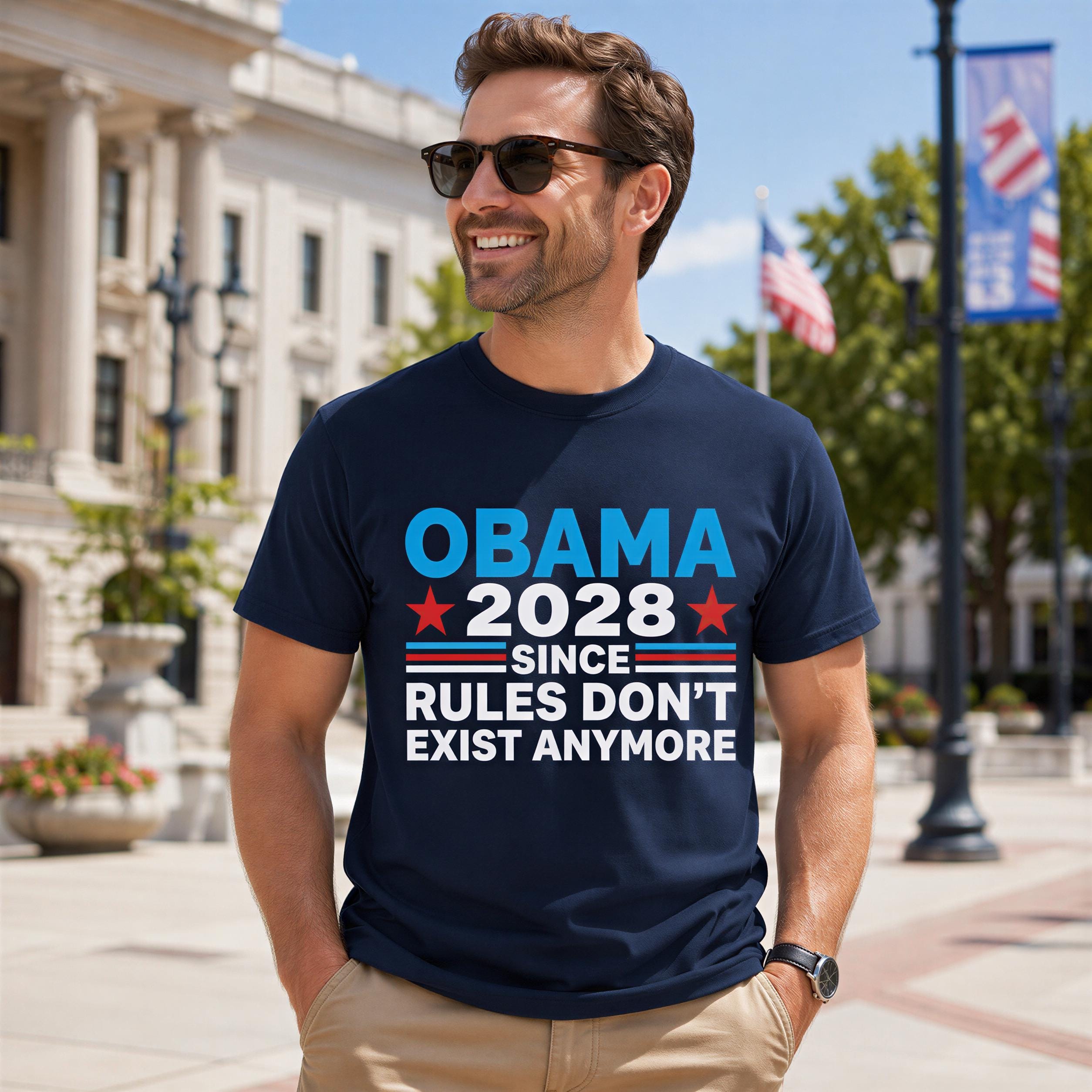 A man wearing a navy blue t-shirt with a political statement printed on it, standing in front of a building with American flags in the background.