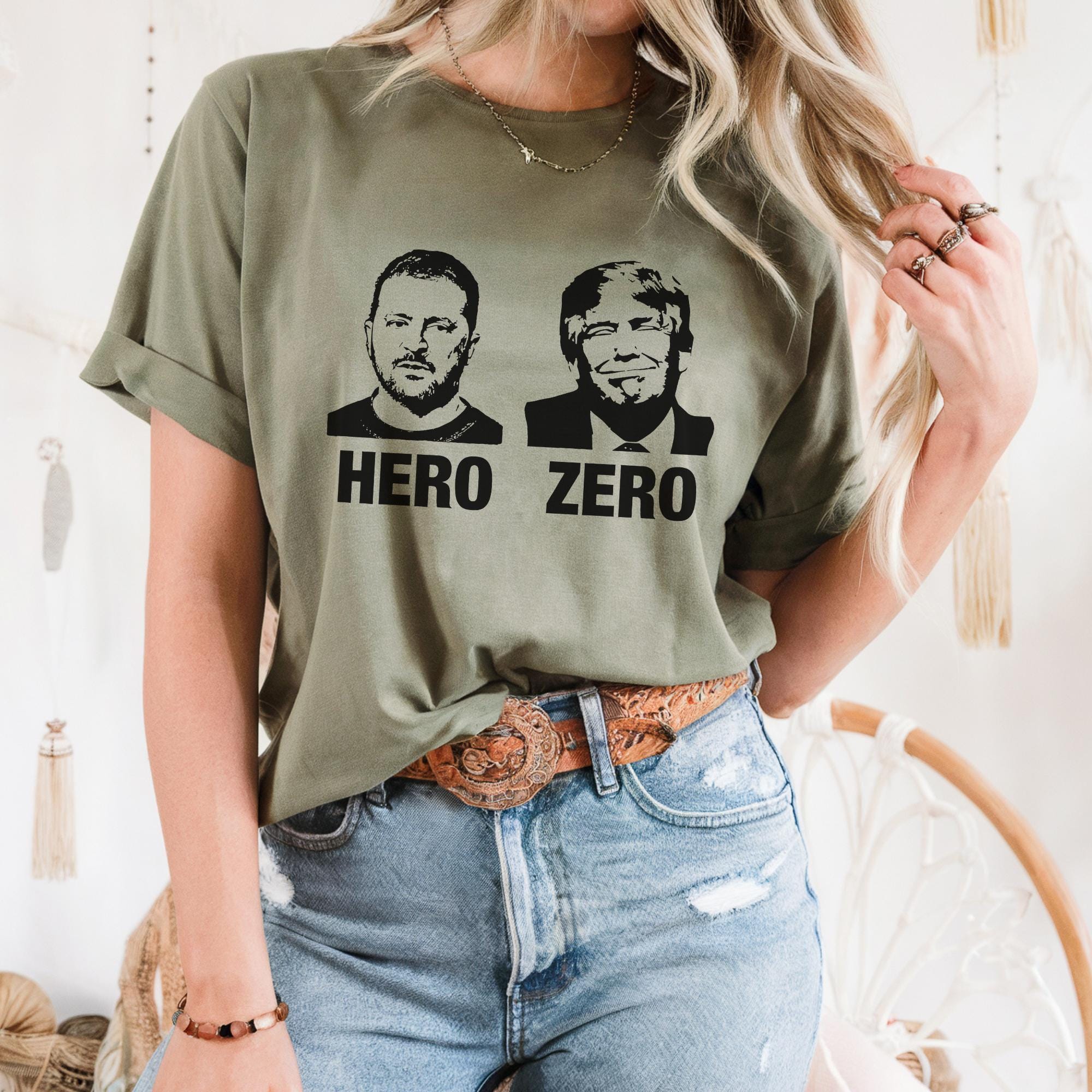 A person wearing a green t-shirt with two black-and-white portraits of men, one labeled "HERO" and the other "ZERO", along with a brown belt.