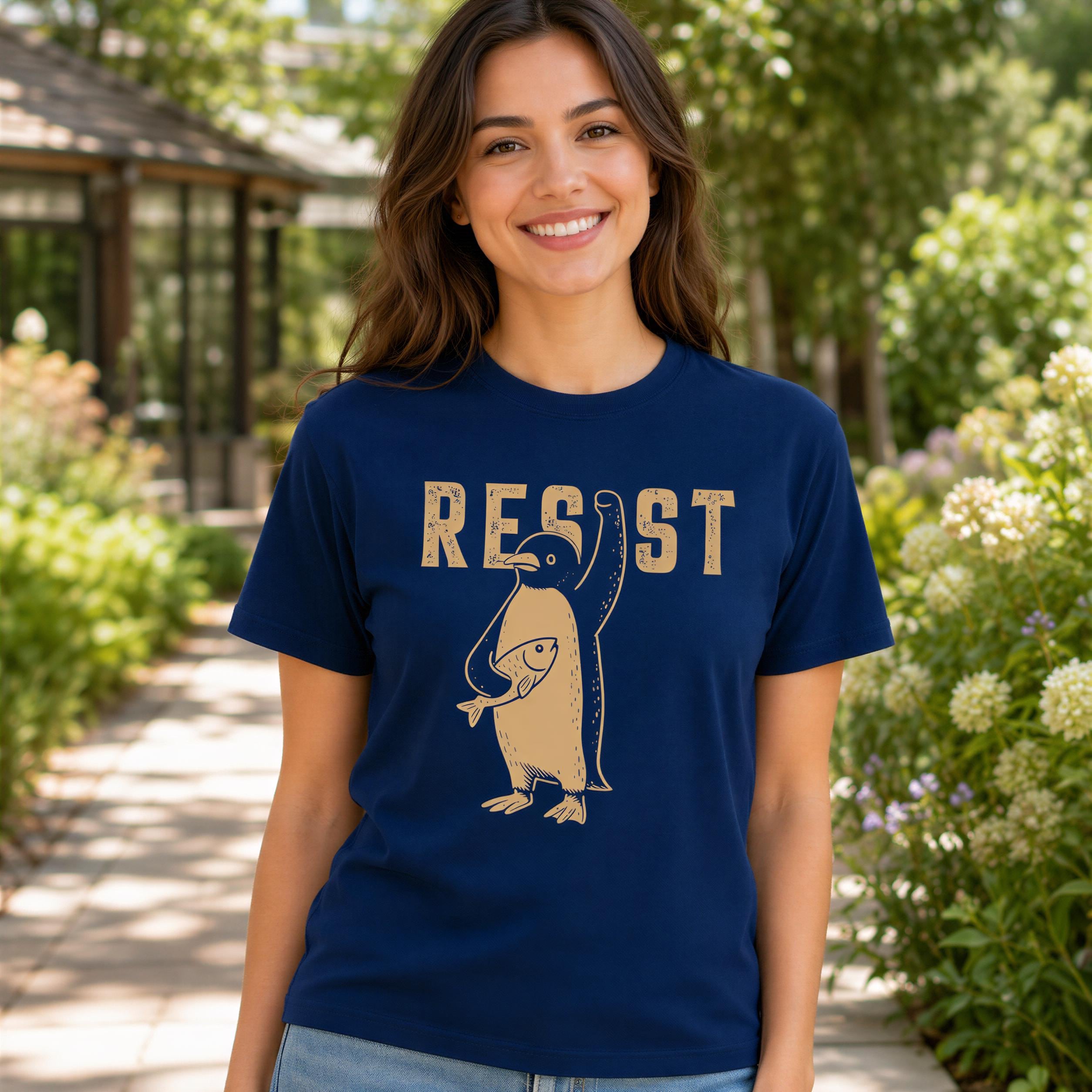 A woman wearing a navy blue t-shirt with a graphic of a penguin and the word "RESIST" printed on it, standing in a garden setting.