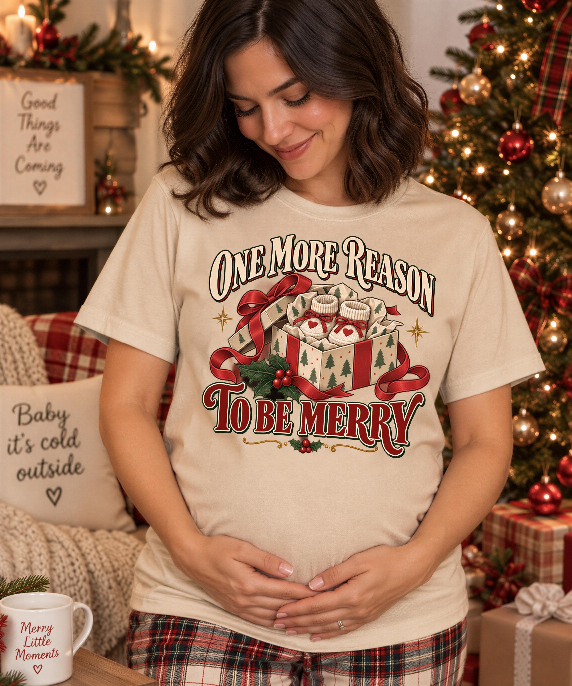 A pregnant woman wearing a t-shirt with a Christmas-themed graphic stands in front of a decorated Christmas tree.