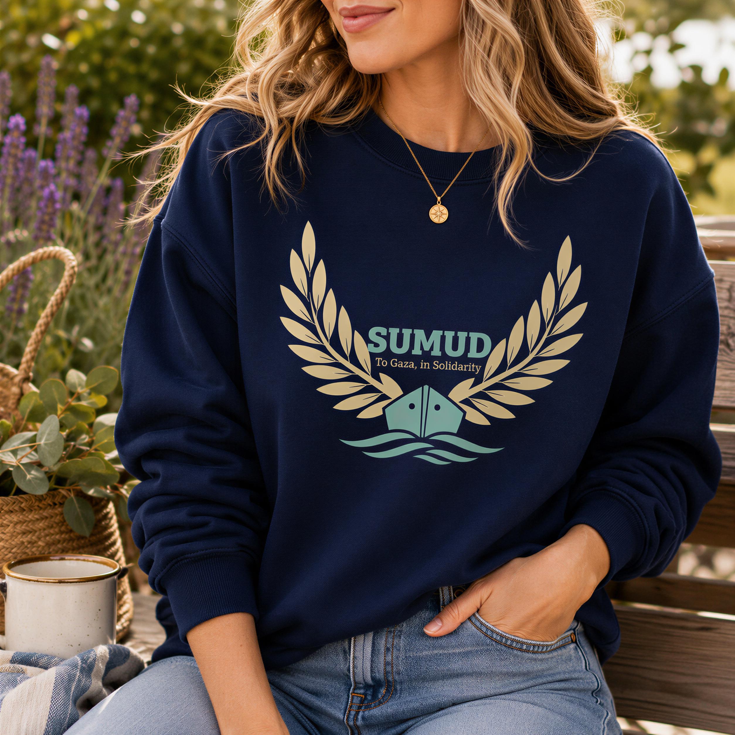 A woman wearing a navy blue sweatshirt with a graphic design and text, sitting on a bench with a potted plant in the background.