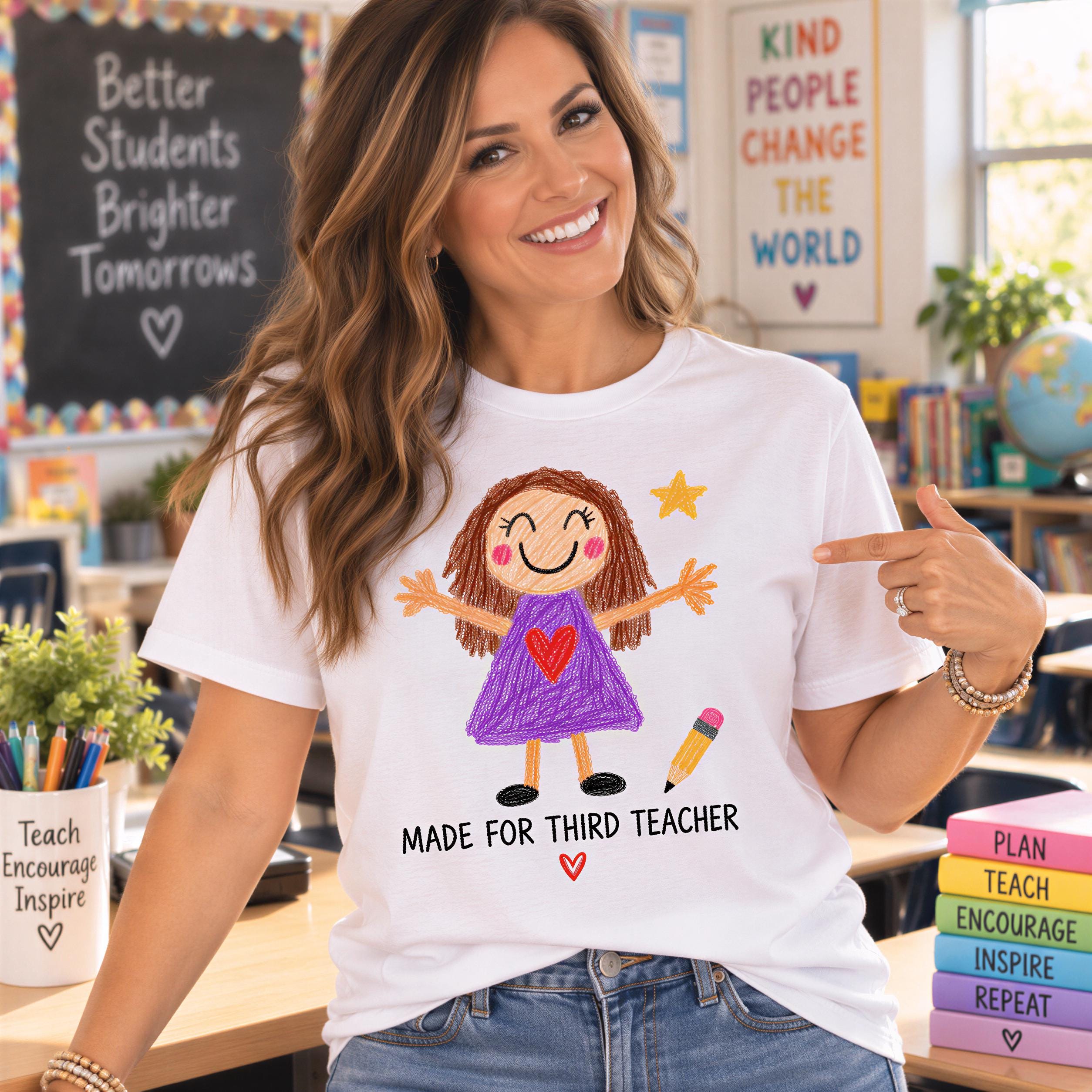 A woman wearing a white t-shirt with a drawing of a smiling girl and the text "MADE FOR THIRD TEACHER" is smiling and pointing at the shirt.