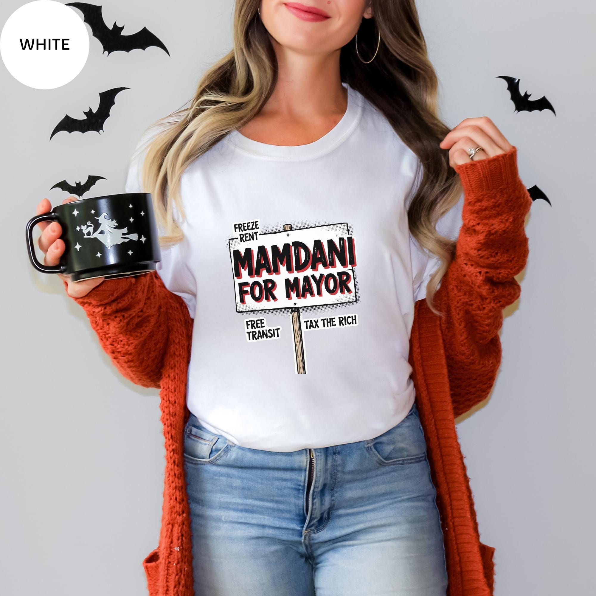 A woman wearing a white t-shirt with a political campaign sign and holding a mug, standing against a wall with bats.