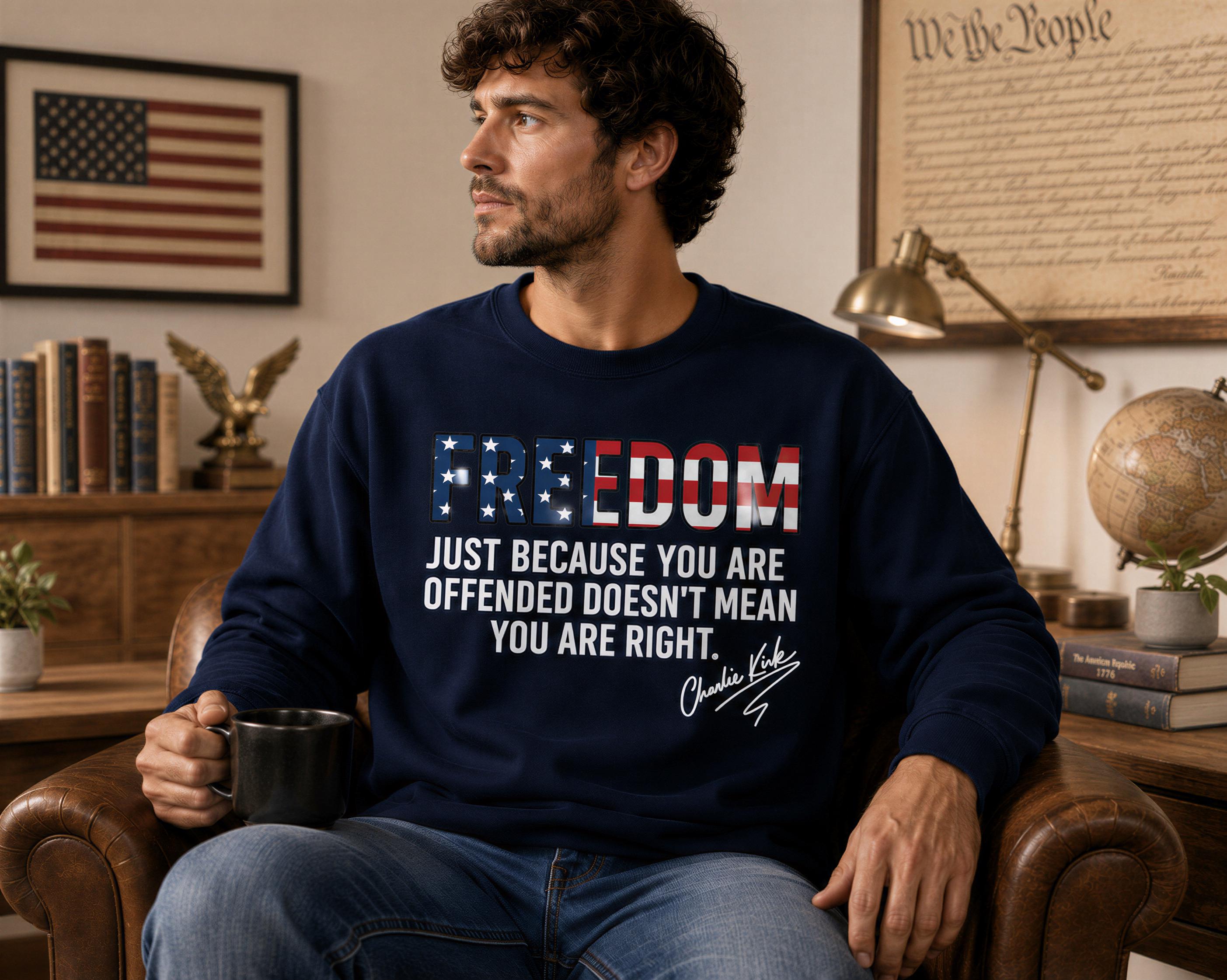 A man wearing a navy blue sweatshirt with the text "FREEDOM" and "JUST BECAUSE YOU ARE OFFENDED DOESN'T MEAN YOU ARE RIGHT" is sitting in a chair, holding a coffee mug.