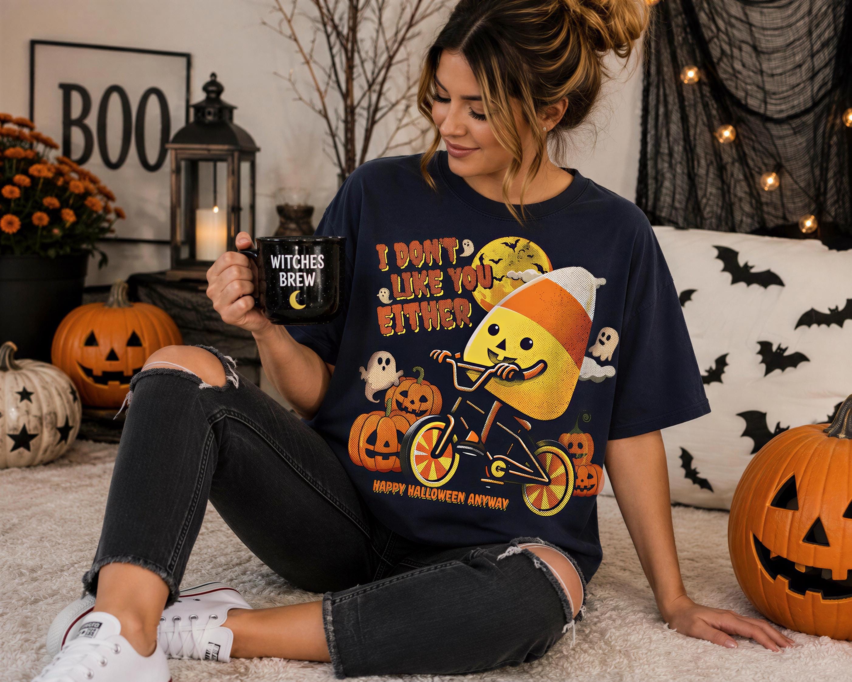 A woman sitting on the floor, holding a mug with a Halloween-themed design, surrounded by jack-o-lanterns and a Halloween-themed decoration.