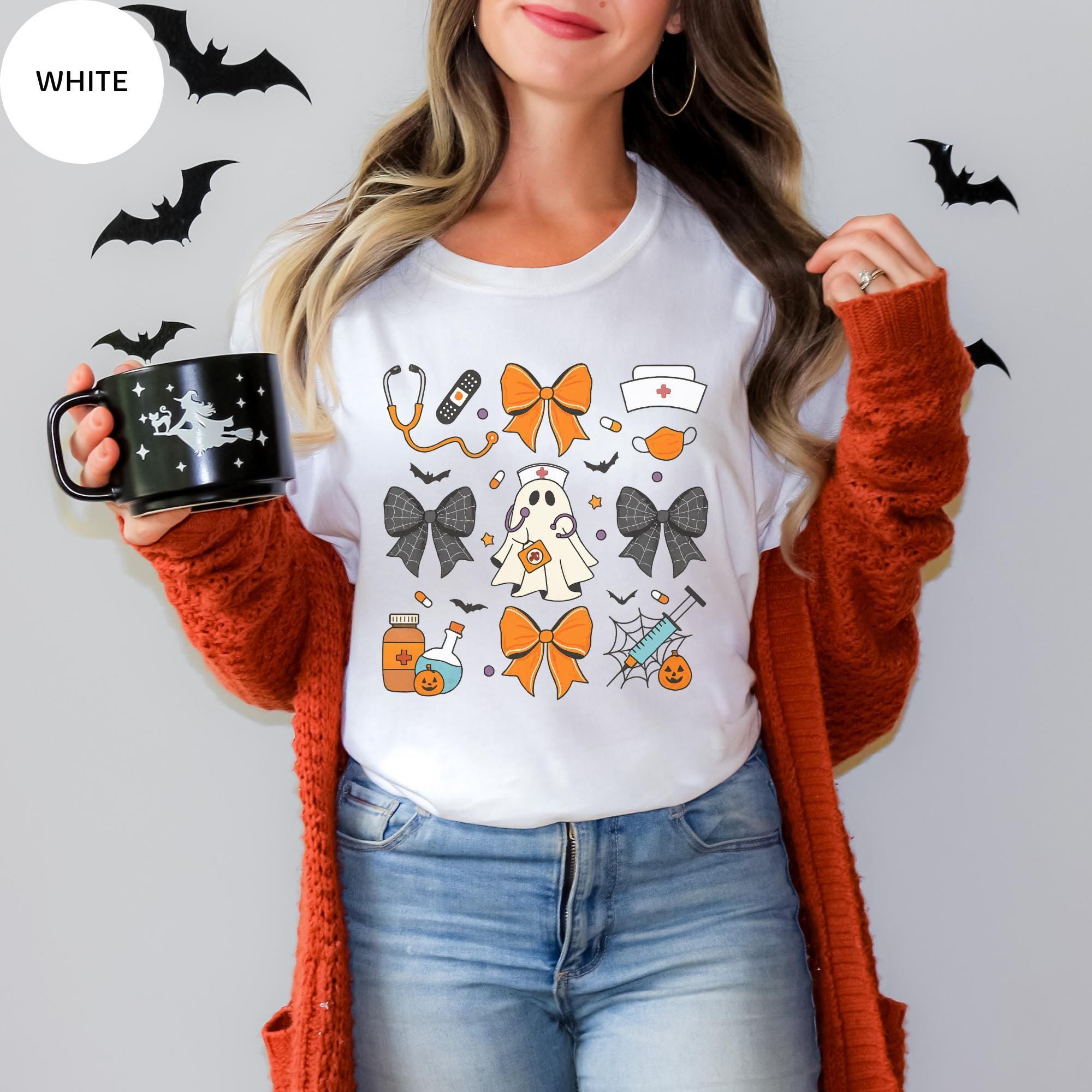 A woman wearing a white t-shirt with Halloween-themed illustrations and holding a black mug with a Halloween design.