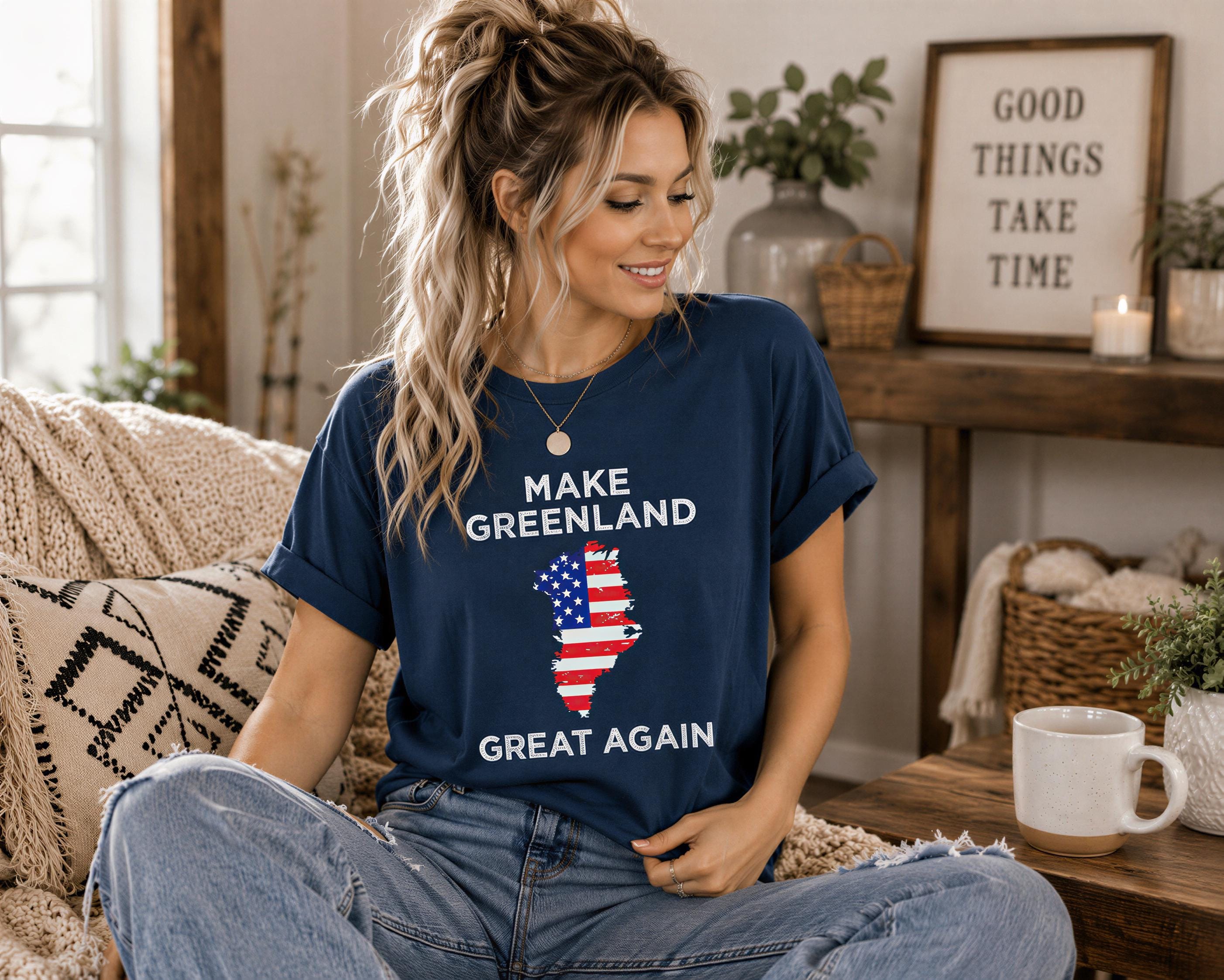 A woman wearing a blue t-shirt with a graphic of the United States and Greenland, sitting on a couch with a coffee mug in front of her.