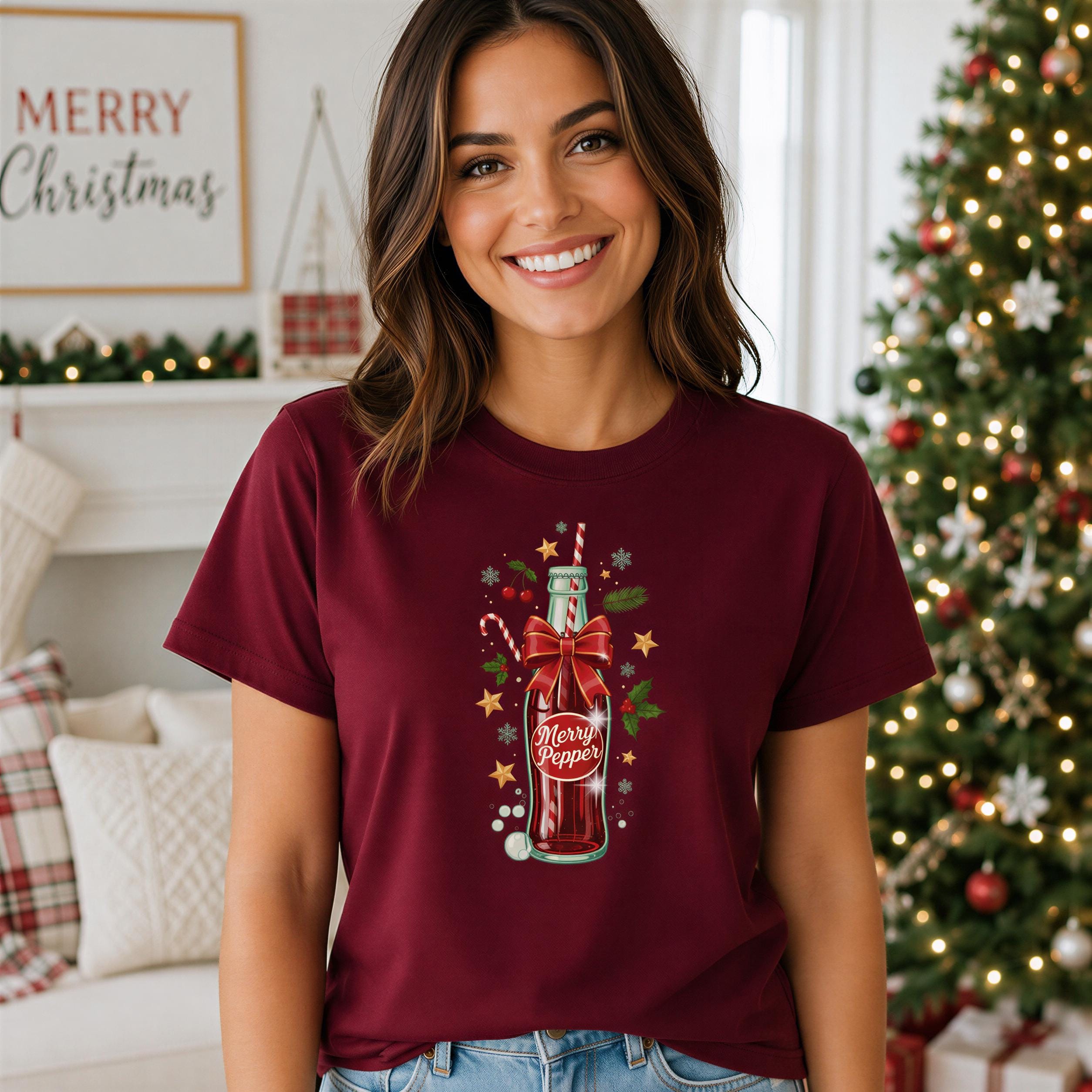 A woman wearing a burgundy t-shirt with a graphic of a bottle of soda and Christmas decorations, smiling at the camera.