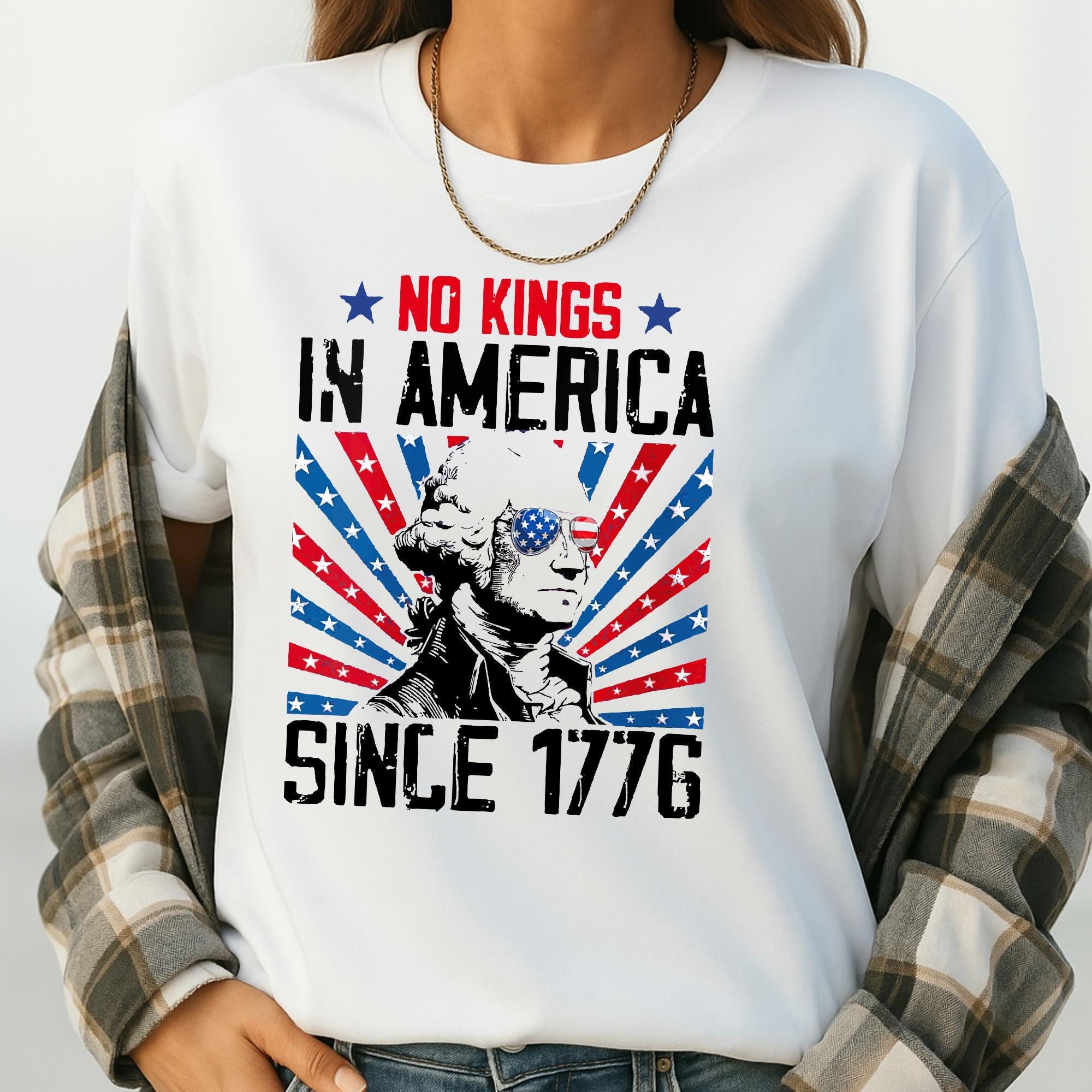 A white t-shirt with a graphic design featuring a portrait of George Washington, the first President of the United States, surrounded by stars and stripes. The text on the t-shirt reads "NO KINGS IN AMERICA SINCE 1776".