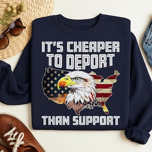 Könnte beinhalten: Marineblaues Sweatshirt mit dem Text "IT'S CHEAPER TO DEPORT THAN SUPPORT". Das Design zeigt eine Karte der amerikanischen Flagge und eine detaillierte Adlerillustration.
