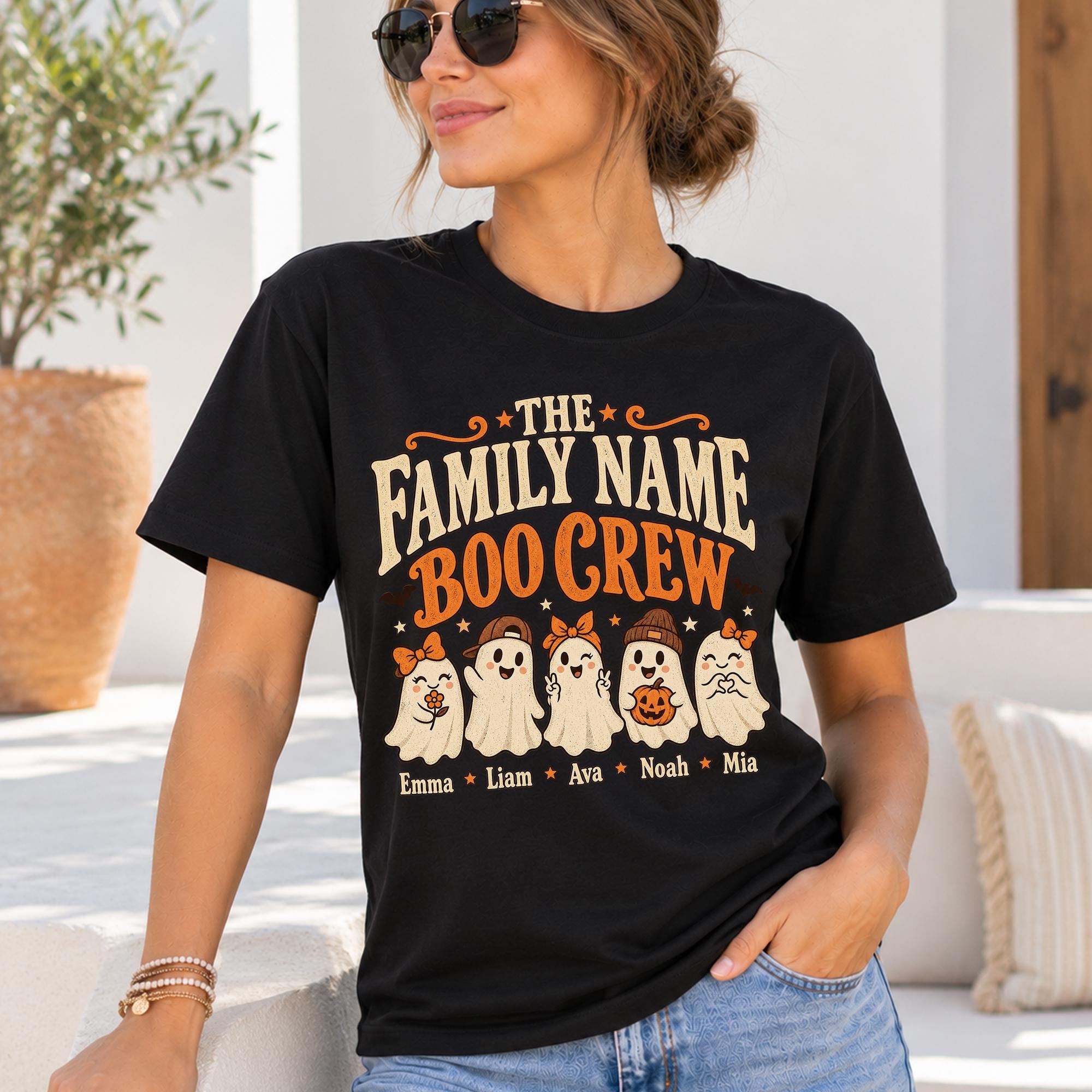A woman wearing a black t-shirt with a graphic design featuring five ghost characters and their names, along with the text "The Family Name Boo Crew".