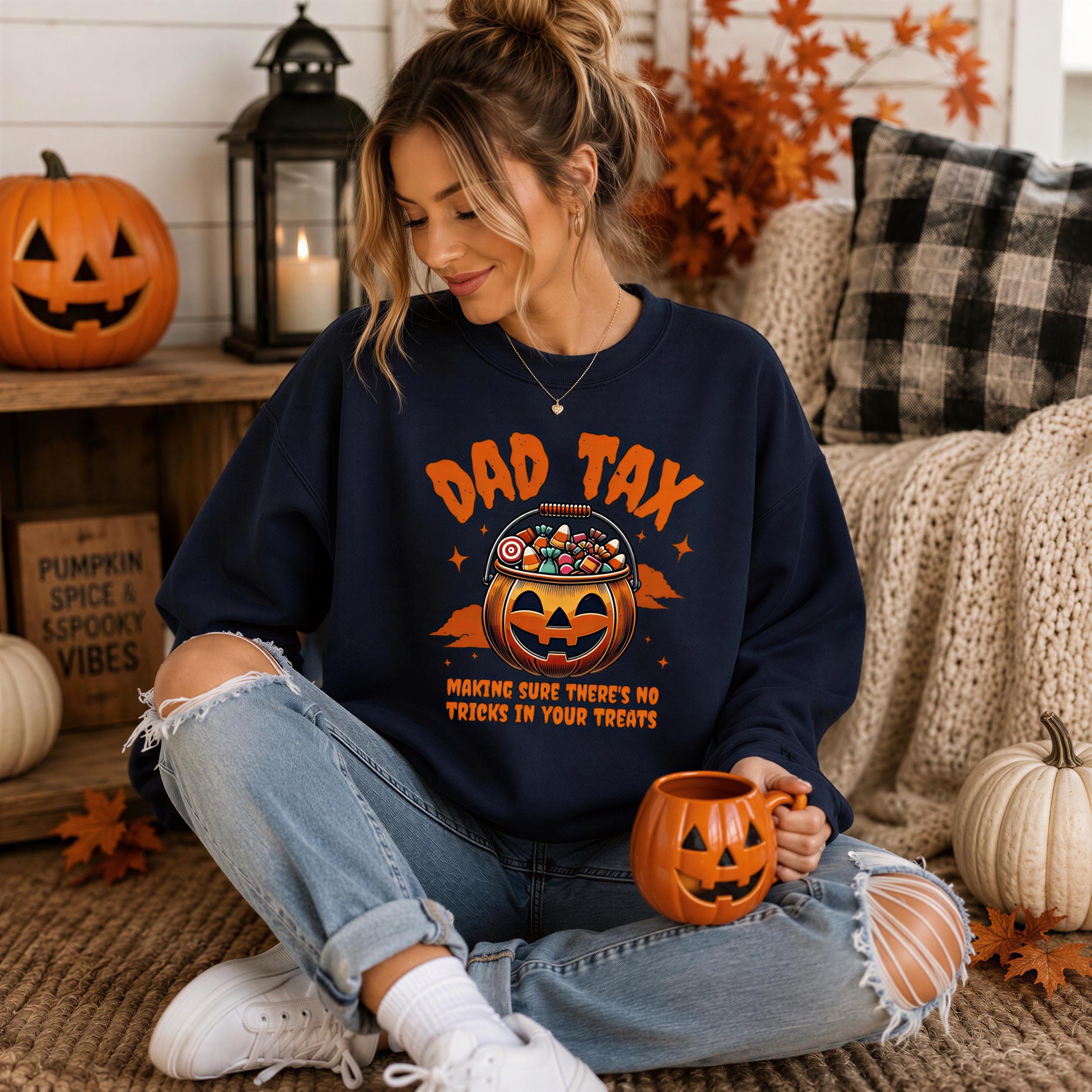 A woman sitting on the floor wearing a navy blue sweatshirt with a pumpkin graphic and text, holding a pumpkin-shaped mug.
