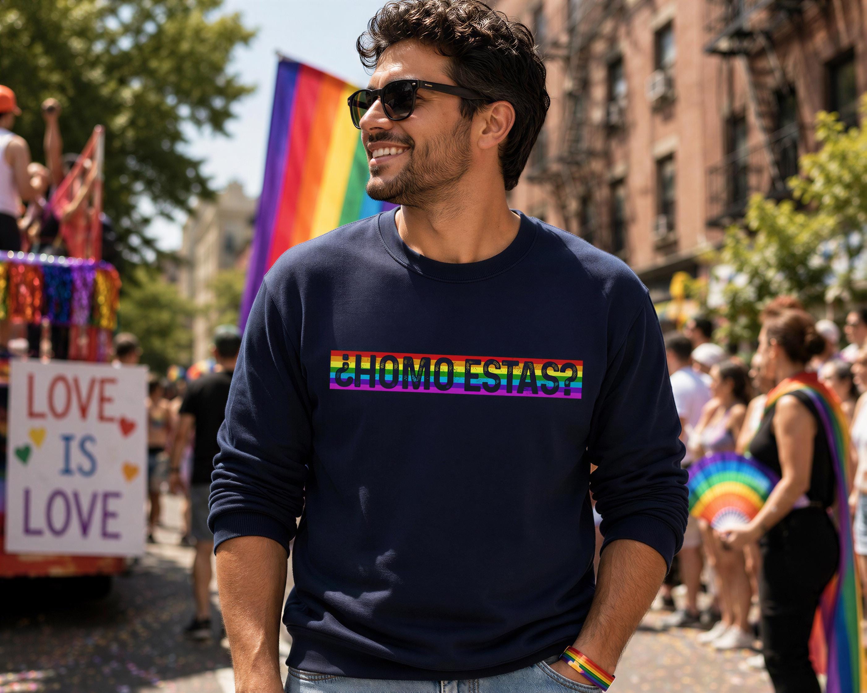 A man wearing a navy blue sweatshirt with rainbow text stands in a crowded parade, surrounded by other participants and colorful floats.