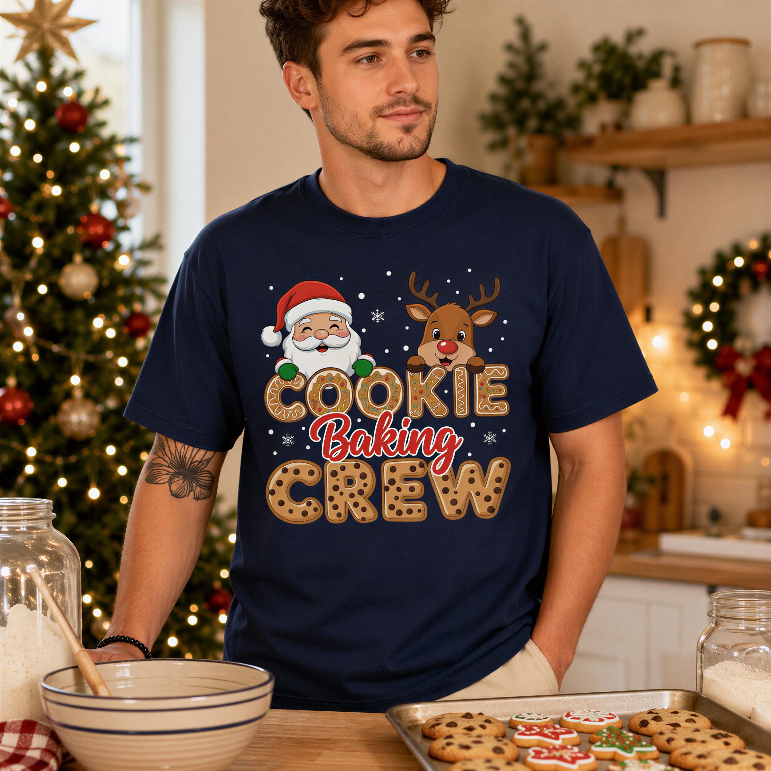 A man wearing a blue t-shirt with a cartoon Santa Claus and a reindeer is standing in a kitchen, with a bowl of cookies and a Christmas tree visible in the background.