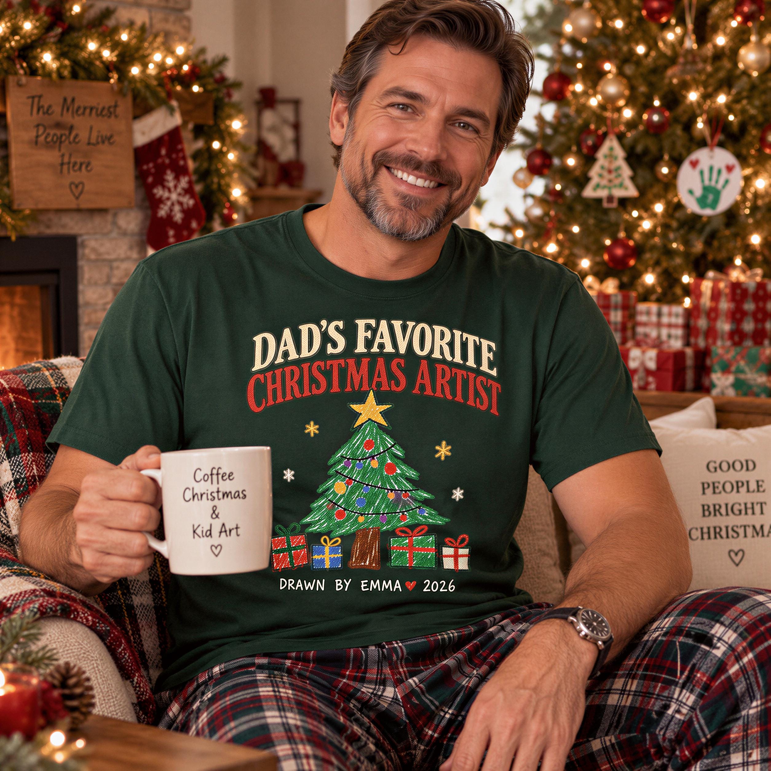 A man wearing a green t-shirt with a Christmas tree design and holding a coffee mug is sitting on a couch in front of a decorated Christmas tree.