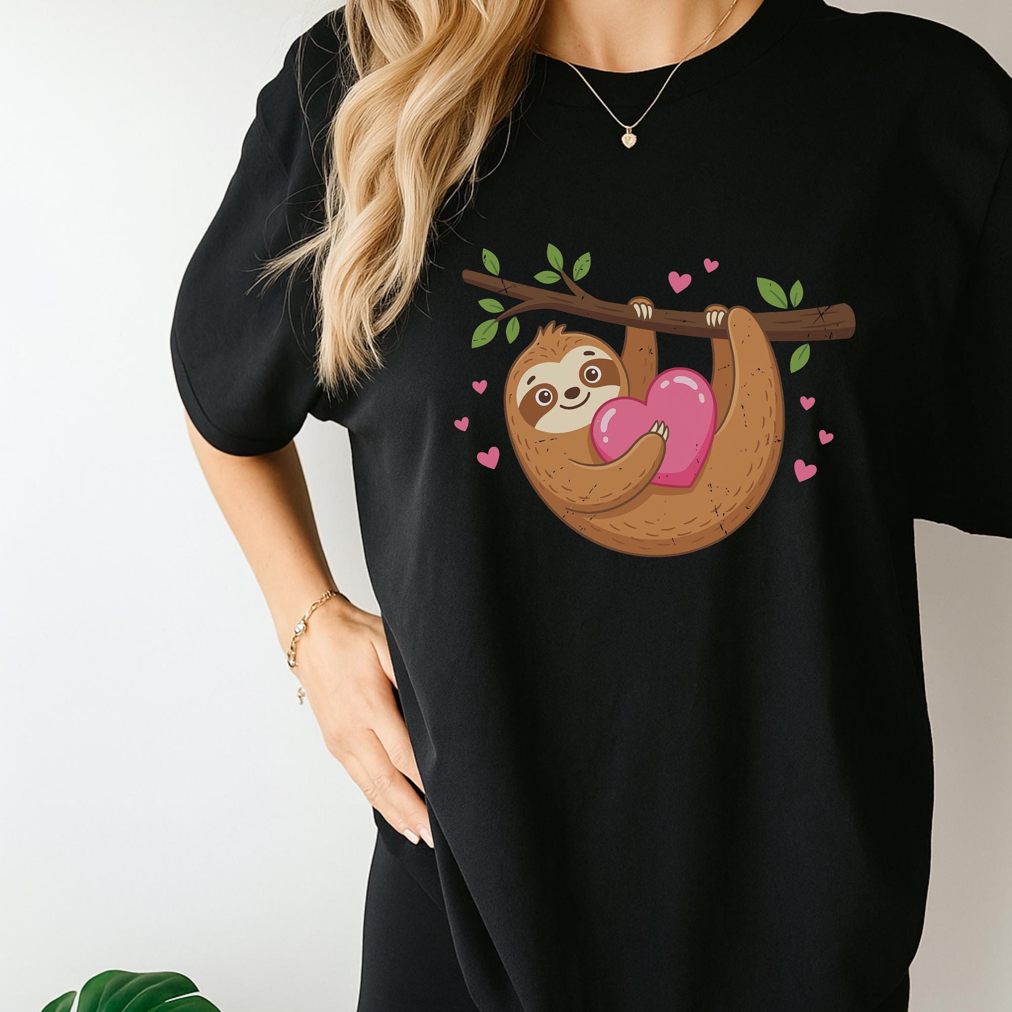 A woman wearing a black t-shirt with a cartoon sloth holding a heart and surrounded by hearts.