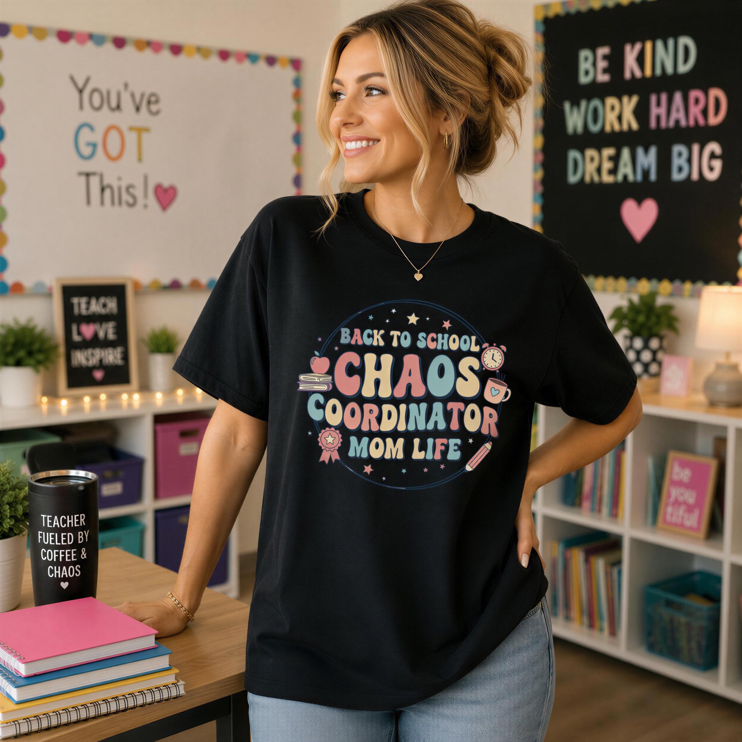 A woman wearing a black t-shirt with a colorful design stands in a classroom setting, smiling and looking to the side.