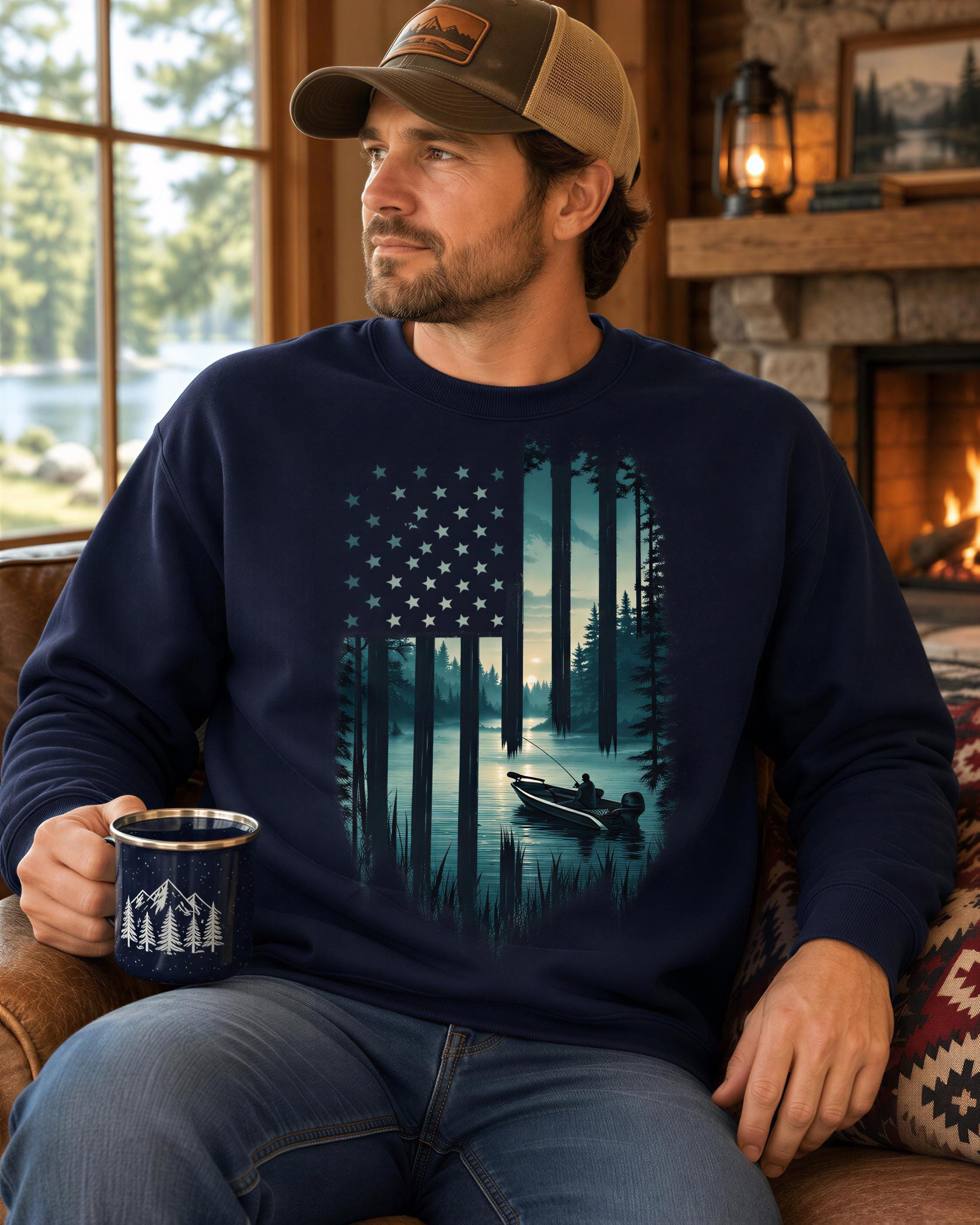 A man wearing a hat and a navy blue sweatshirt with an American flag design is sitting on a couch, holding a mug, and looking out a window.